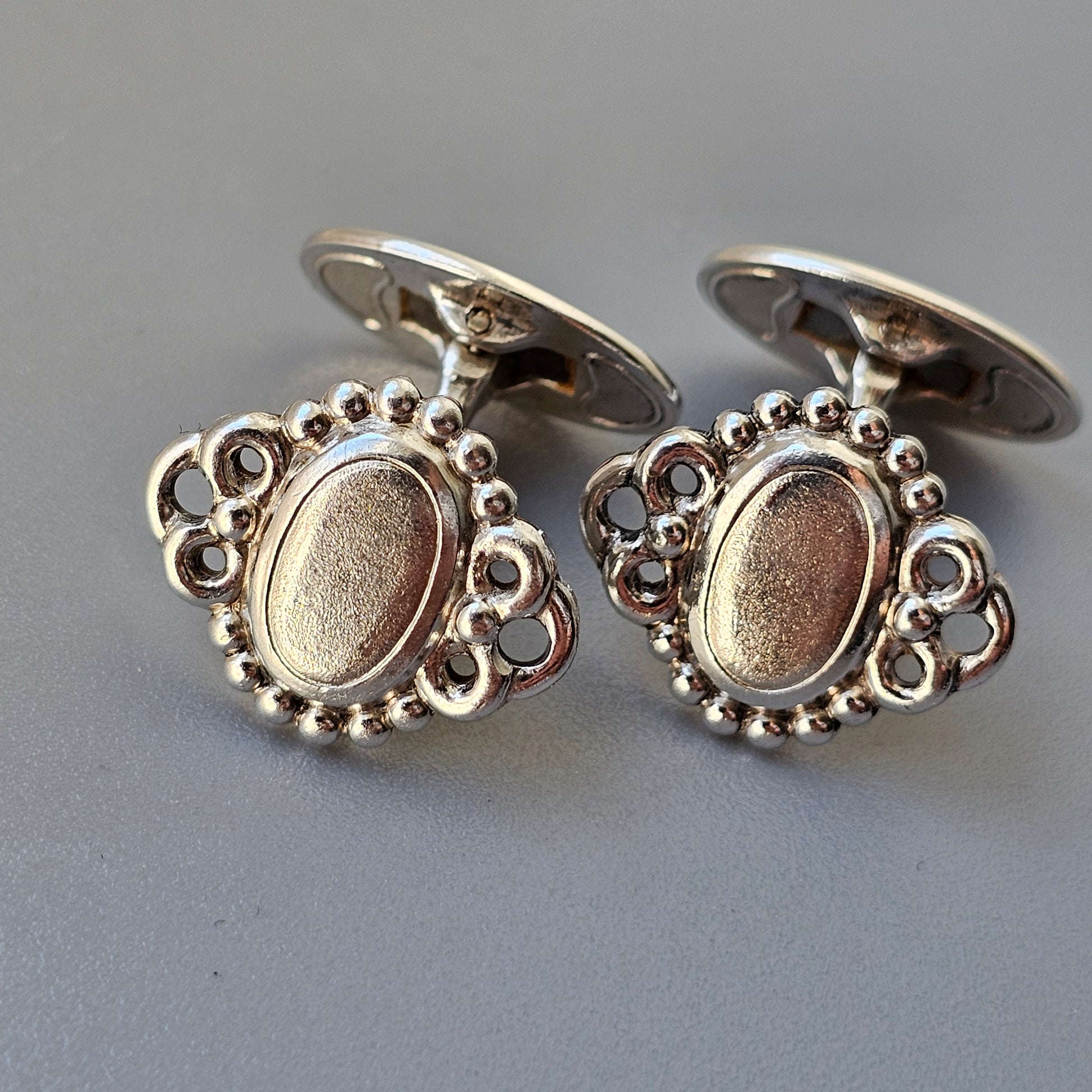 Pair of ornate silver cufflinks with oval centers and decorative beaded edges.