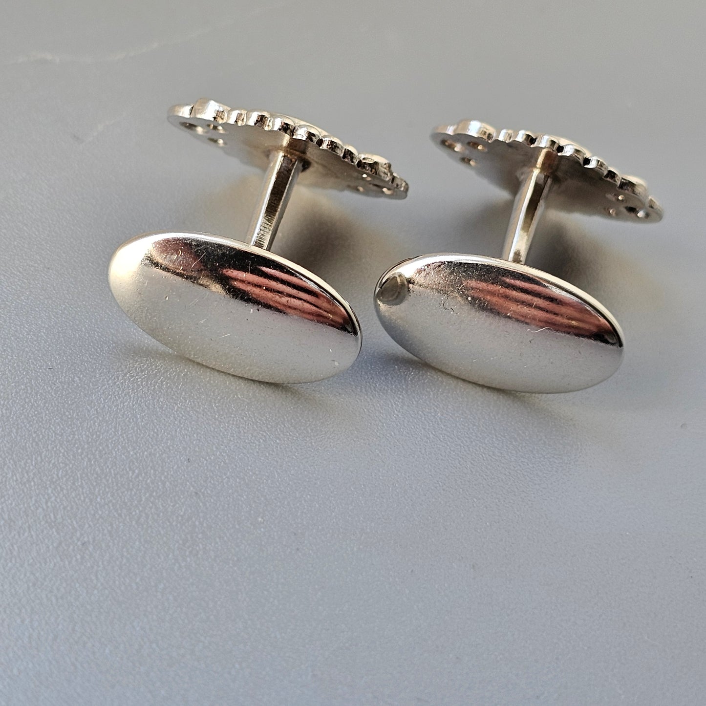 Pair of oval silver cufflinks with decorative edges and a reddish accent.