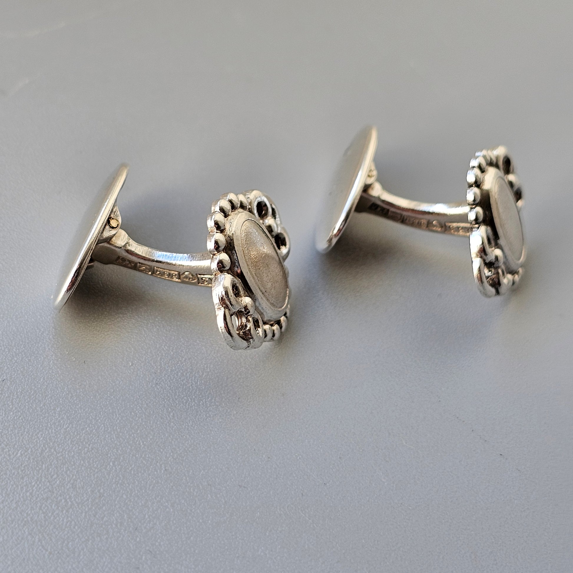 Pair of silver cufflinks with oval-shaped mother-of-pearl centers surrounded by decorative borders.