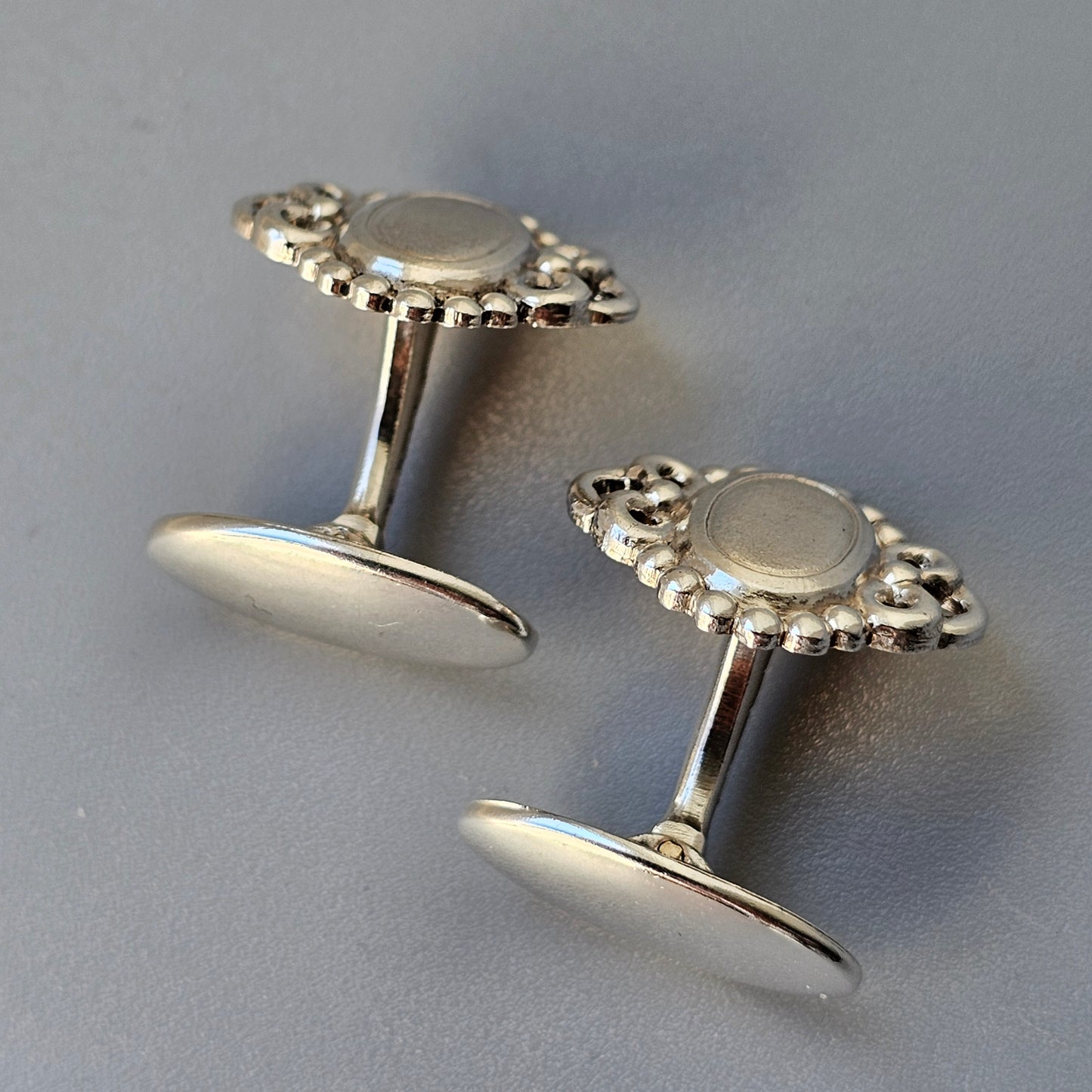 Pair of ornate silver cufflinks with floral-like designs.