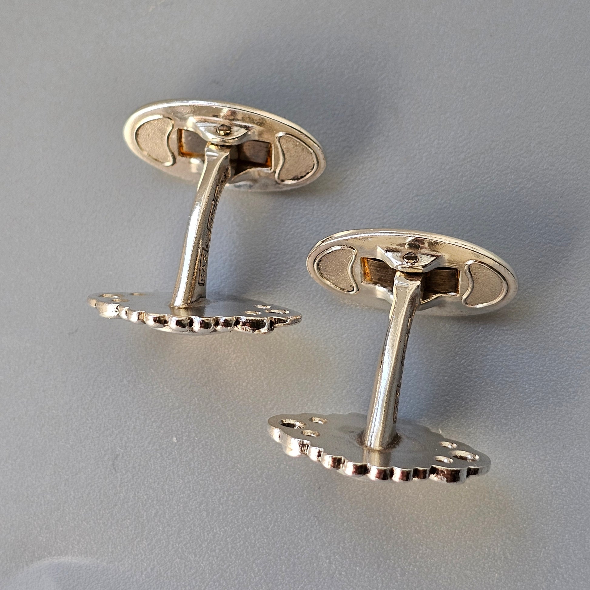 Pair of silver-colored cufflinks shaped like bicycle gears.