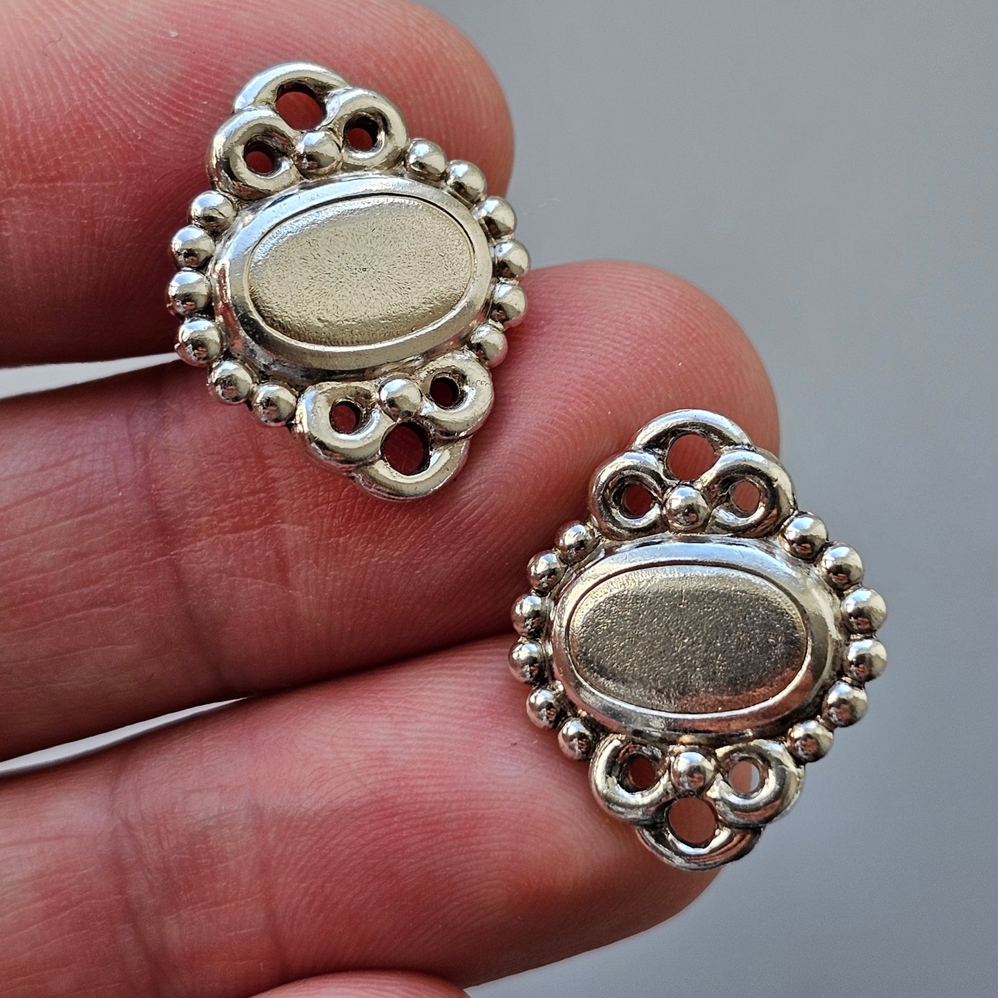 Silver earrings with oval centers and decorative filigree edges.