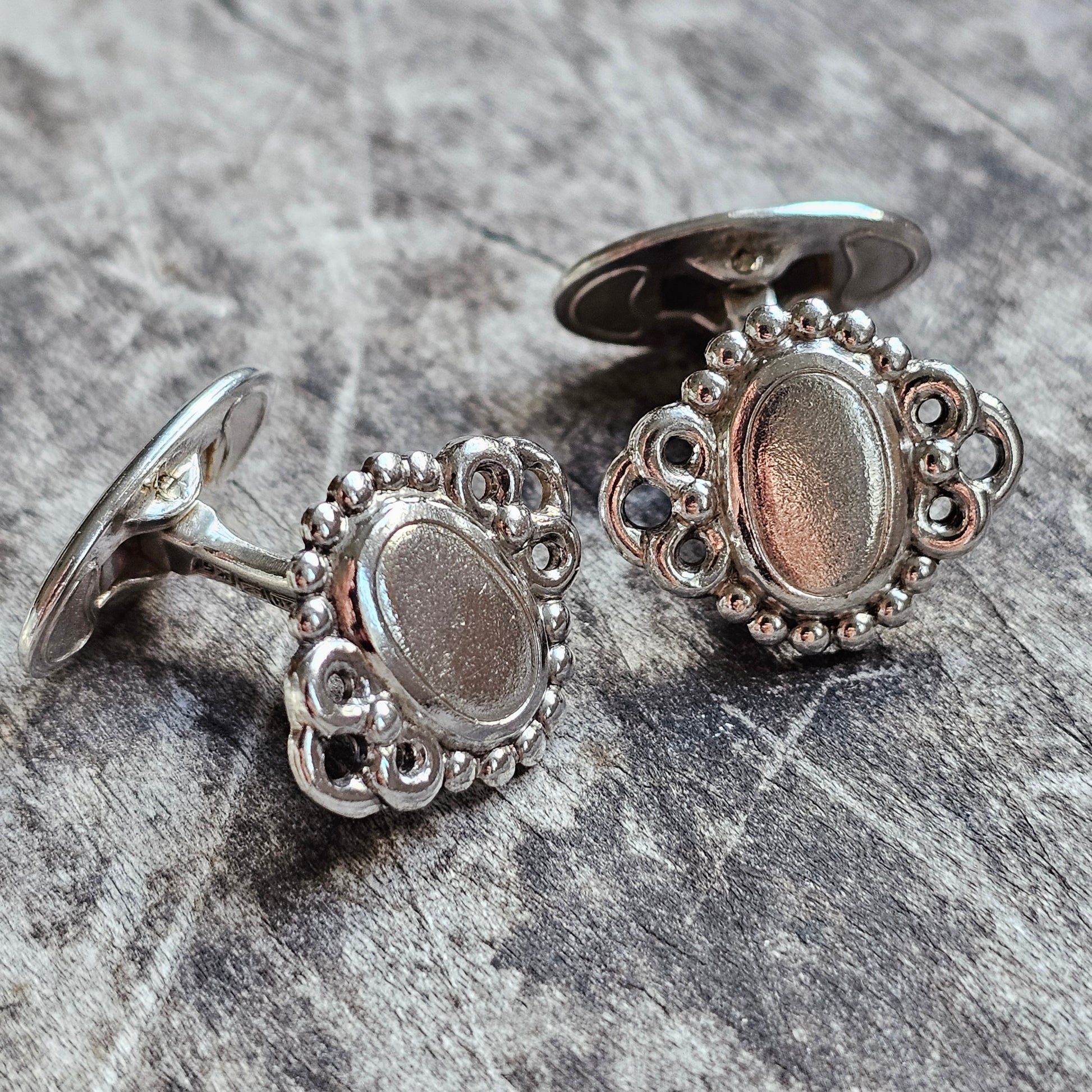 Pair of ornate silver cufflinks with oval centers and decorative beaded edges.