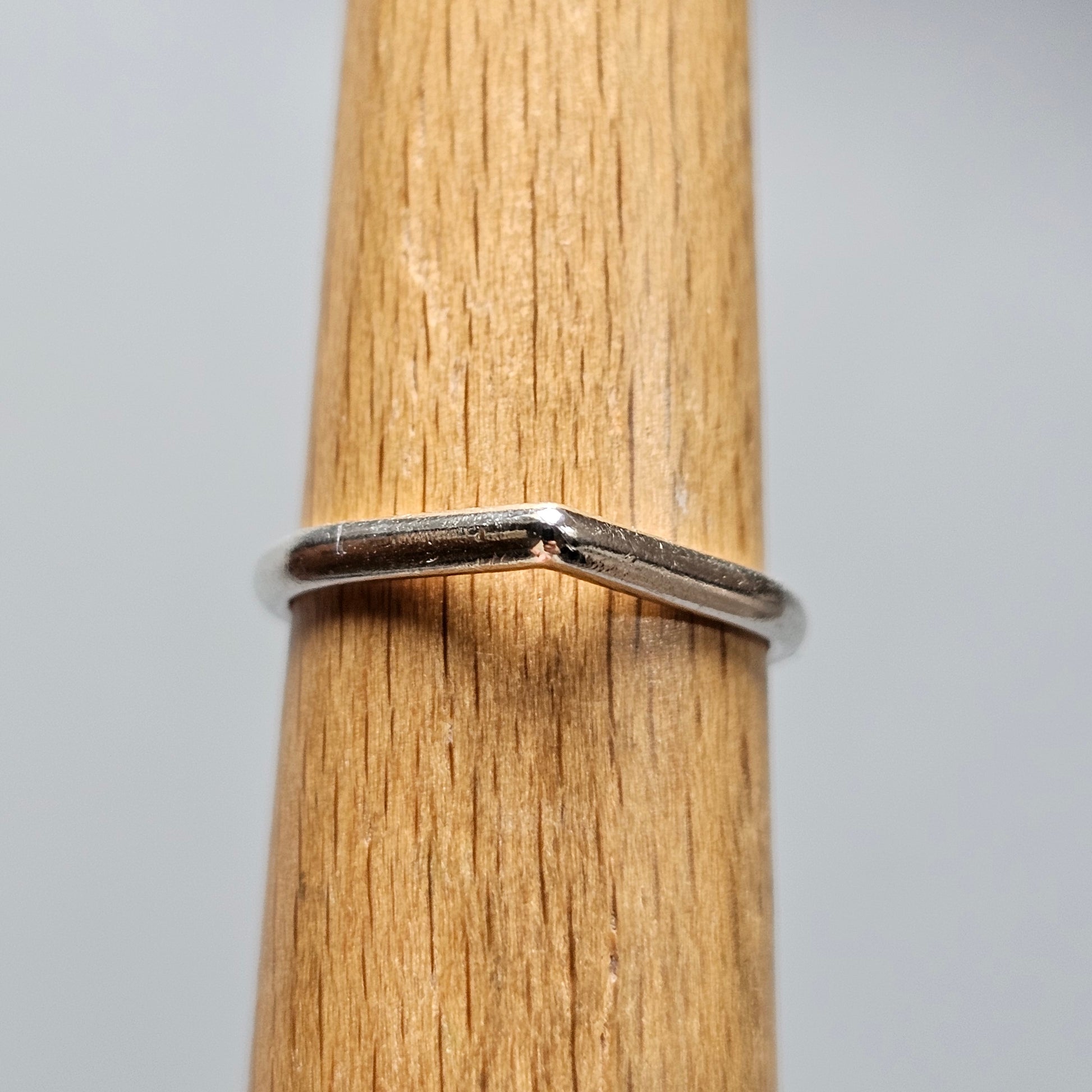 Silver ring with a subtle V-shaped design on a wooden surface.