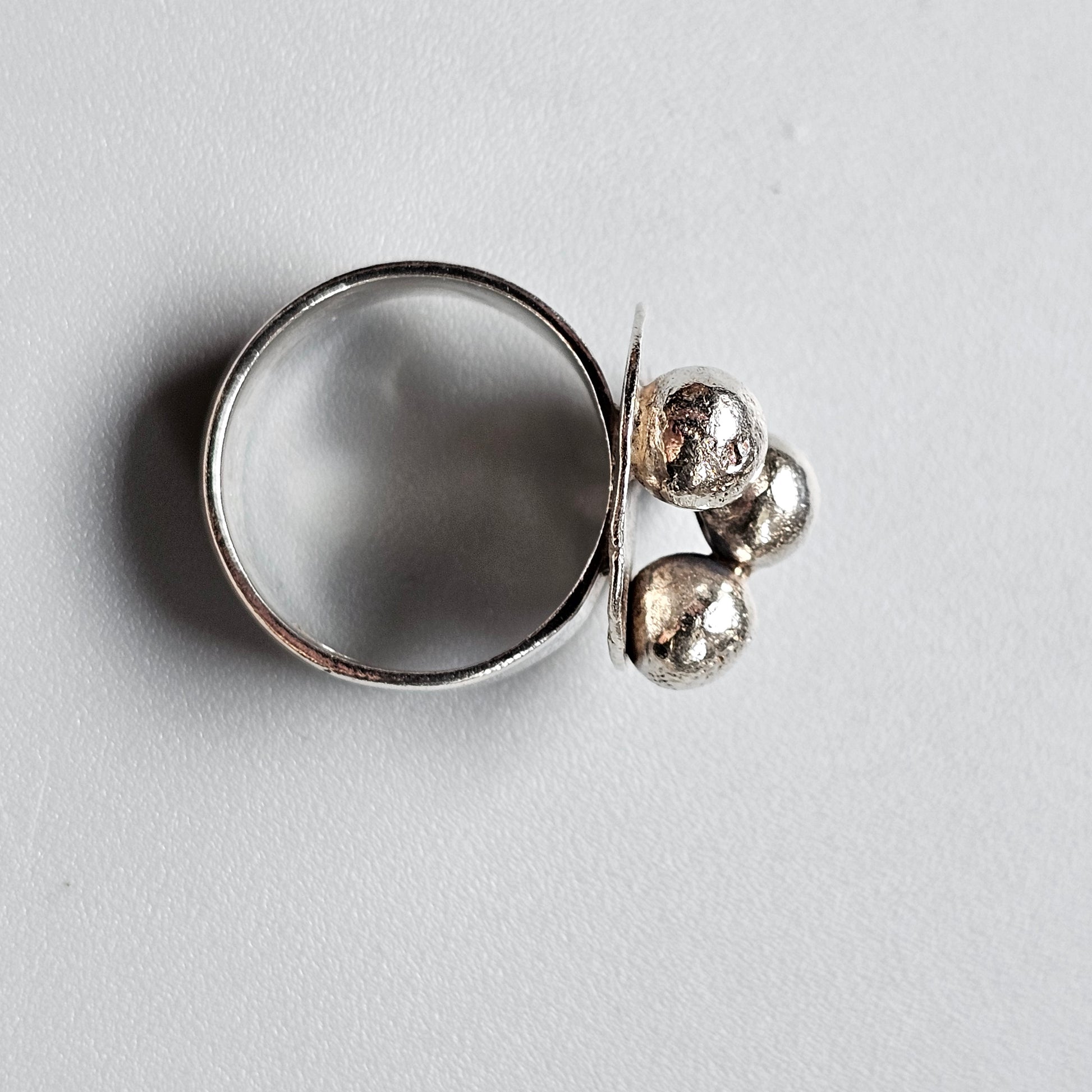 Silver ring with a circular flat surface and three small spherical attachments.