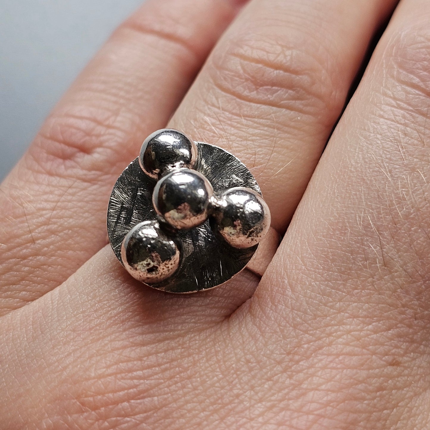 Unique silver ring featuring four spherical beads on a textured circular base.