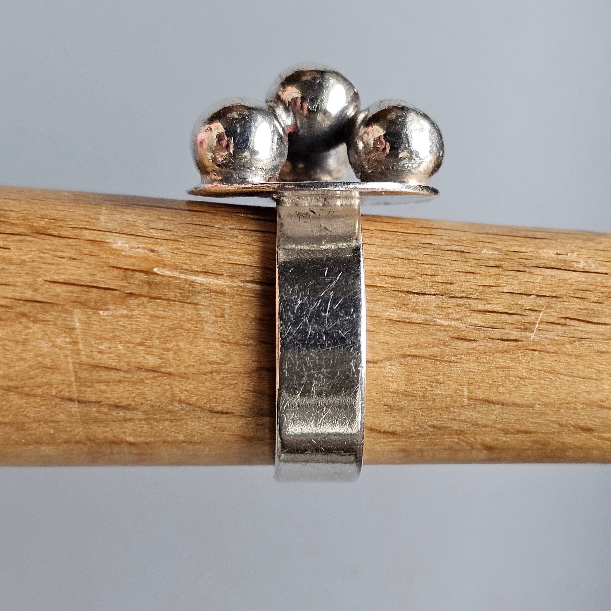 Silver ring with three spherical beads atop a flat band, clasped onto a wooden surface.