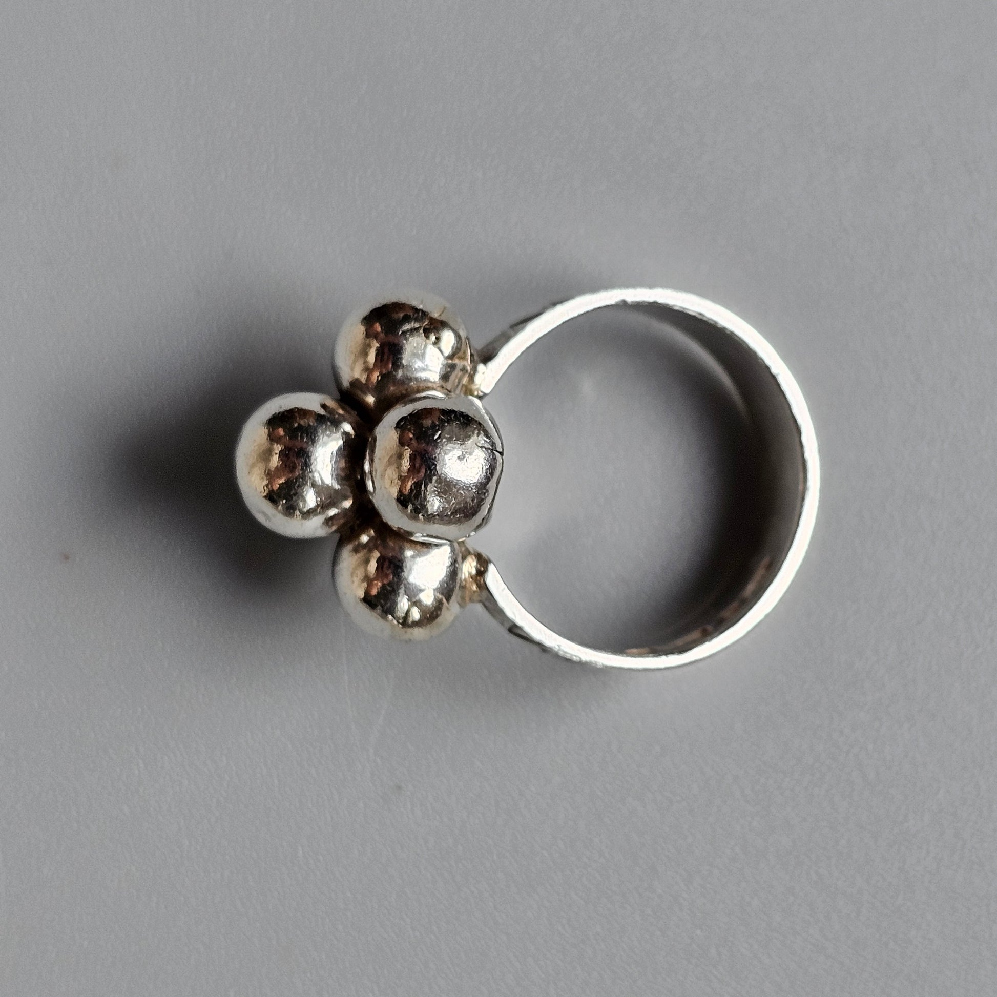 Silver ring with a cluster of four rounded metallic elements forming a floral-like design on top.