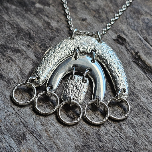 Silver pendant necklace featuring a crescent shape with dangling rings.