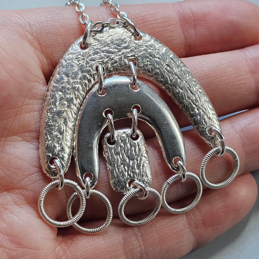 Silver pendant necklace with textured crescent shapes and dangling rings.