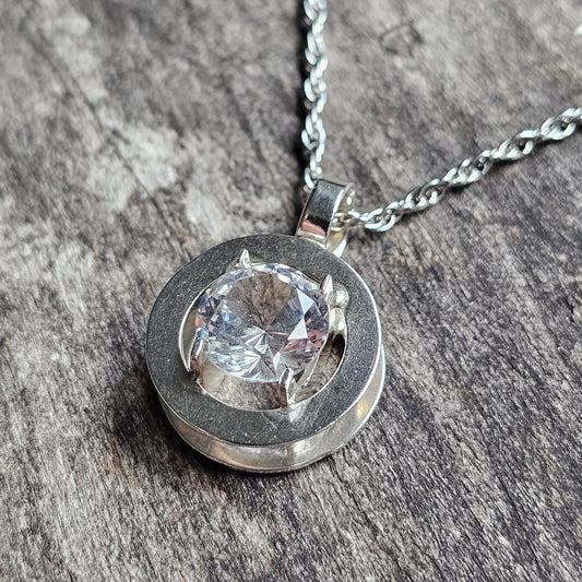 Silver pendant necklace featuring a round setting with a clear gemstone.