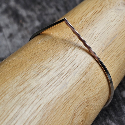 Thin silver bracelet or bangle wrapped around a wooden surface.