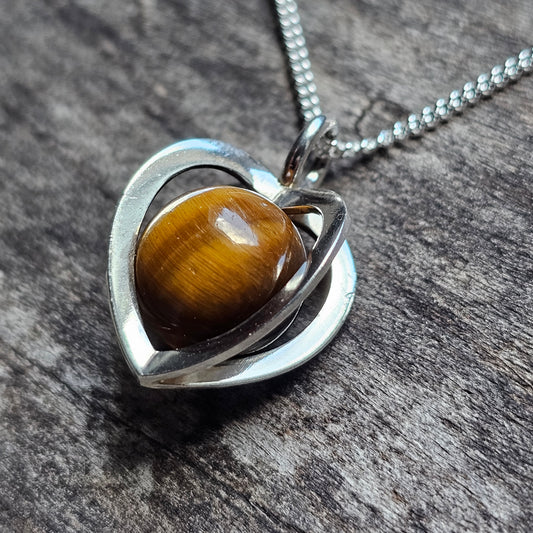 Heart-shaped silver pendant with a tiger’s eye gemstone nestled inside.