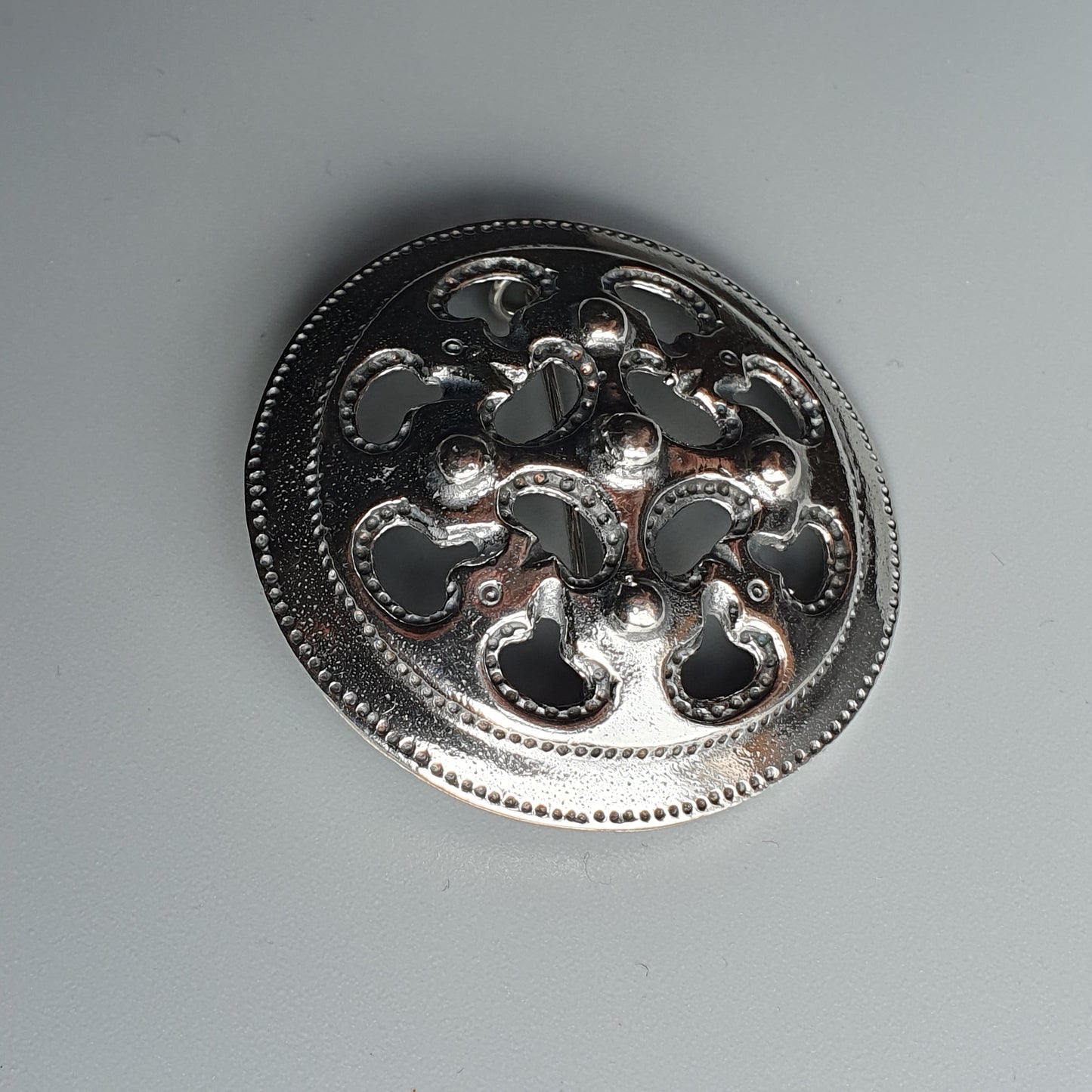 Ornate silver brooch or pin with a circular floral design.