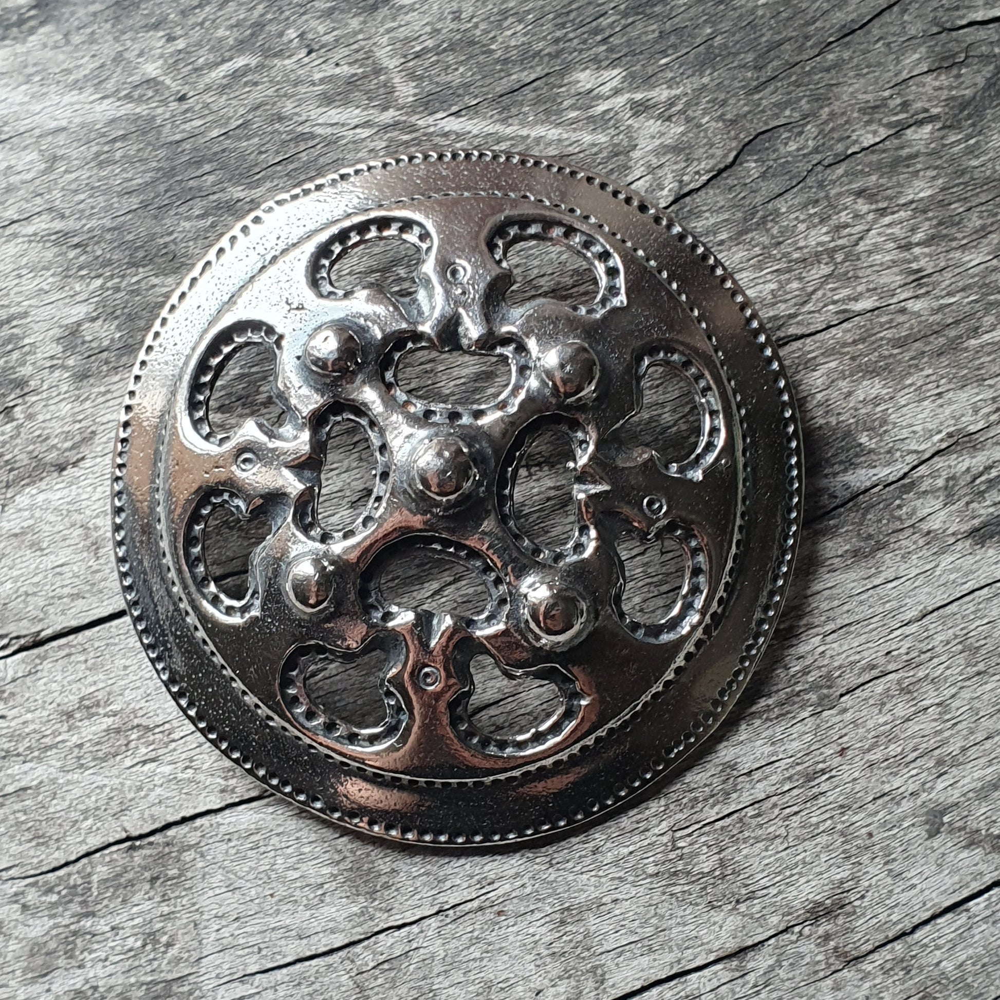 Ornate metal brooch or medallion with a circular design featuring intricate cutouts and raised patterns.