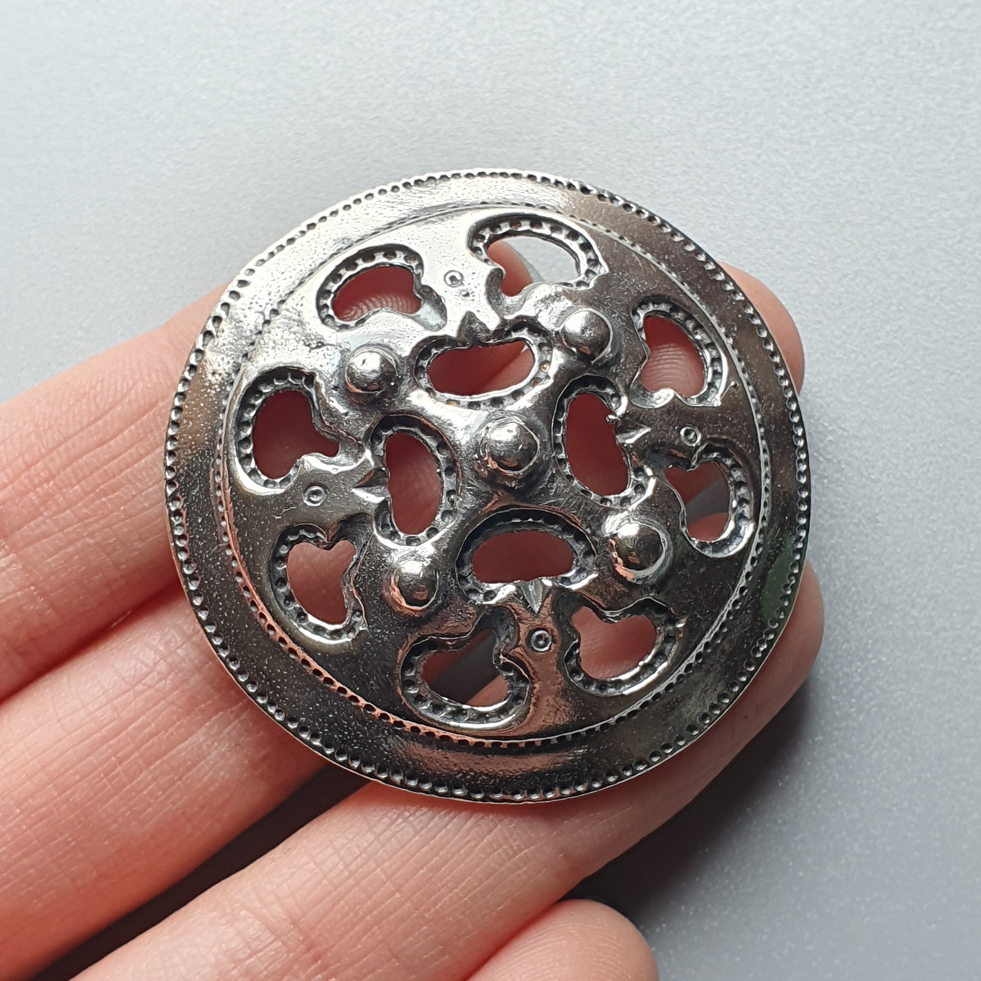 Ornate silver brooch or button with intricate cutout design and red backing.