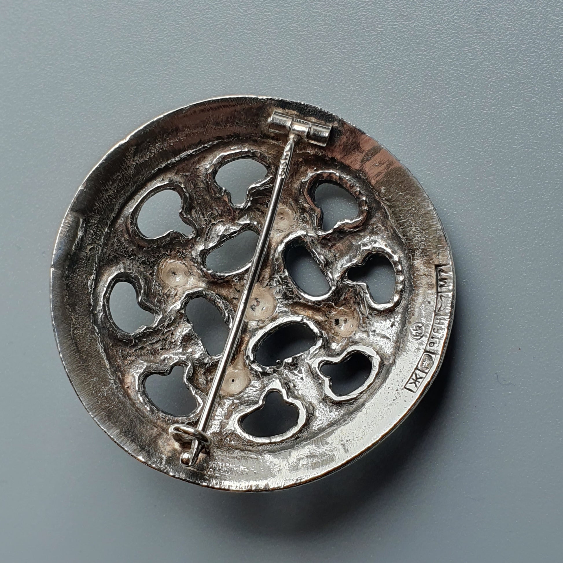 Circular metal brooch with decorative cutout patterns and a central pin.