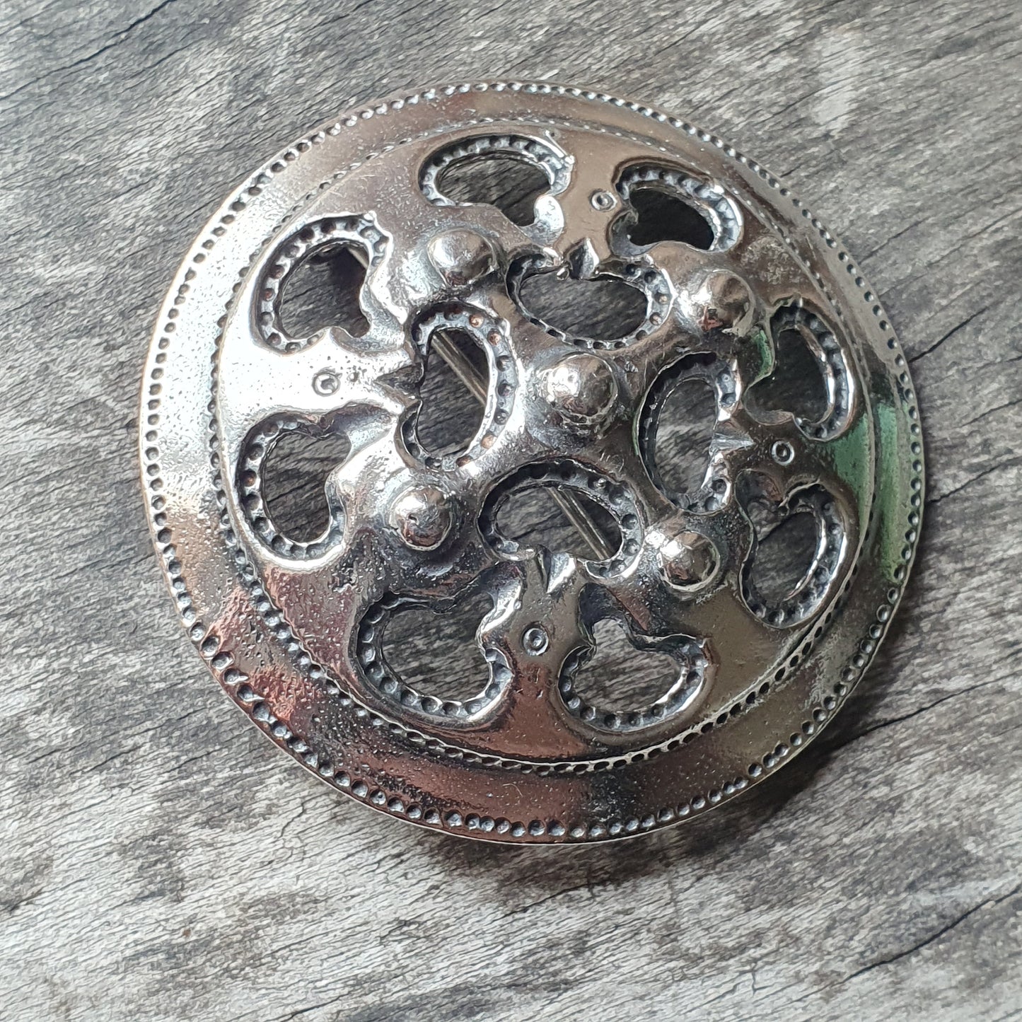 Ornate silver brooch or pendant with a circular shape and intricate cutout design.