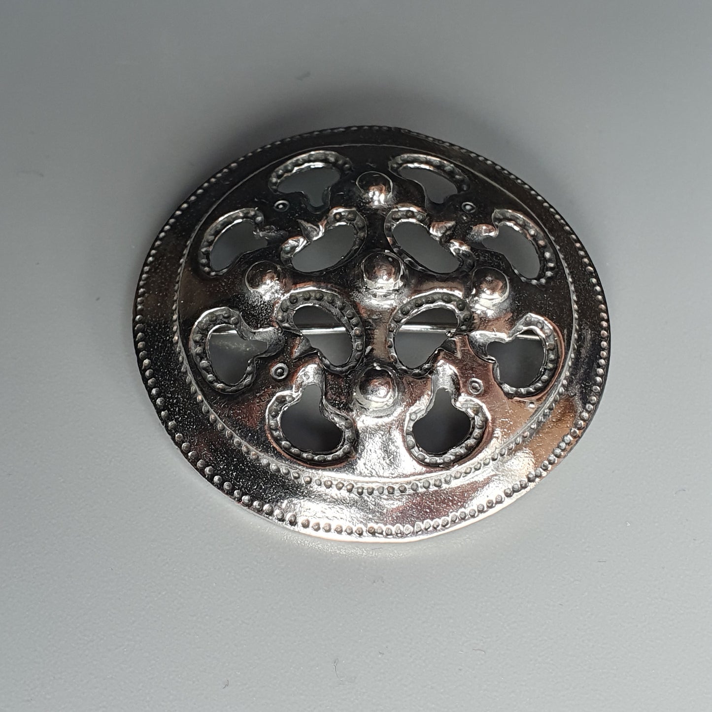 Ornate silver brooch or pendant with a circular floral cutout design.