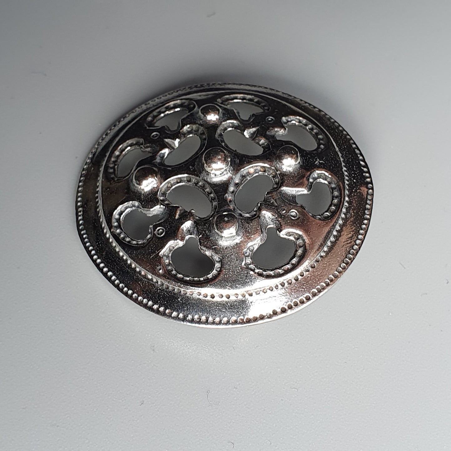 Ornate silver brooch or medallion with a circular design featuring floral or swirling patterns.