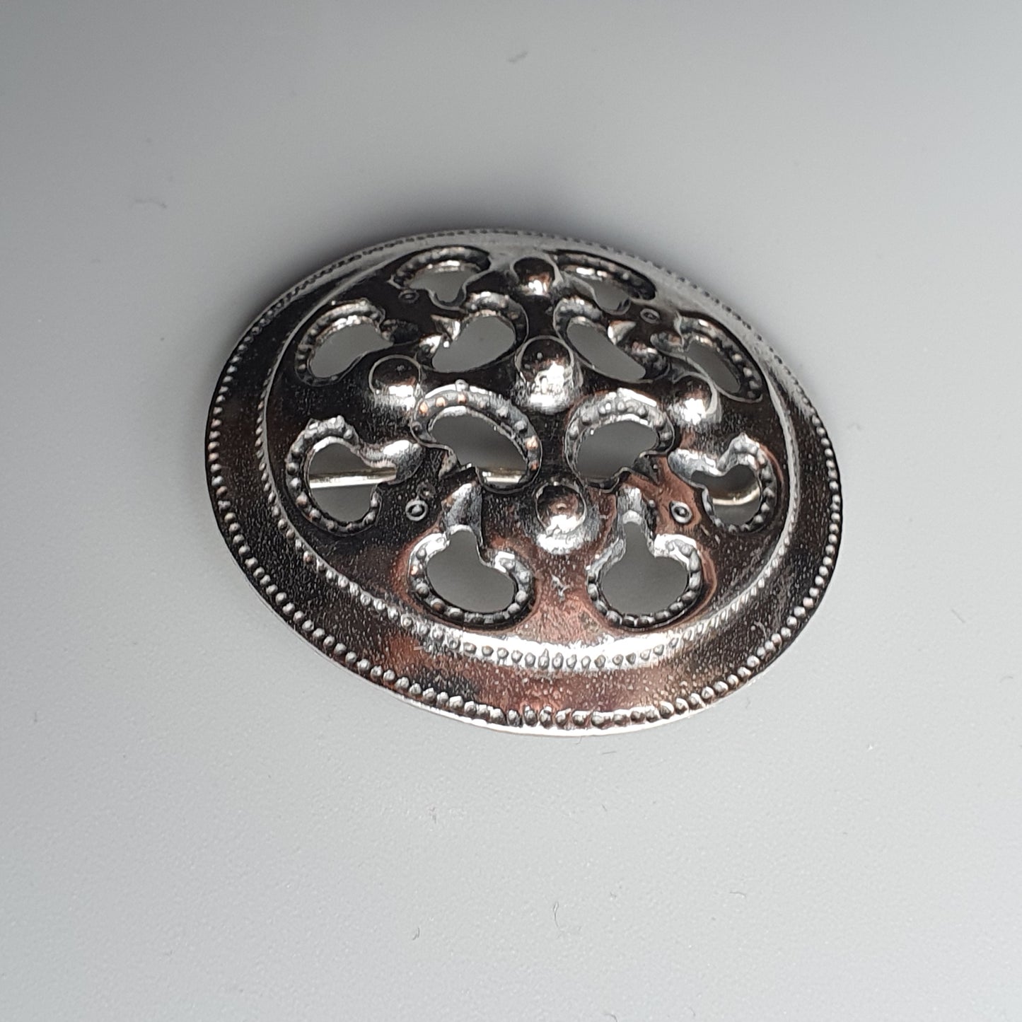 Ornate silver brooch or pendant with a circular shape and intricate cutout design.