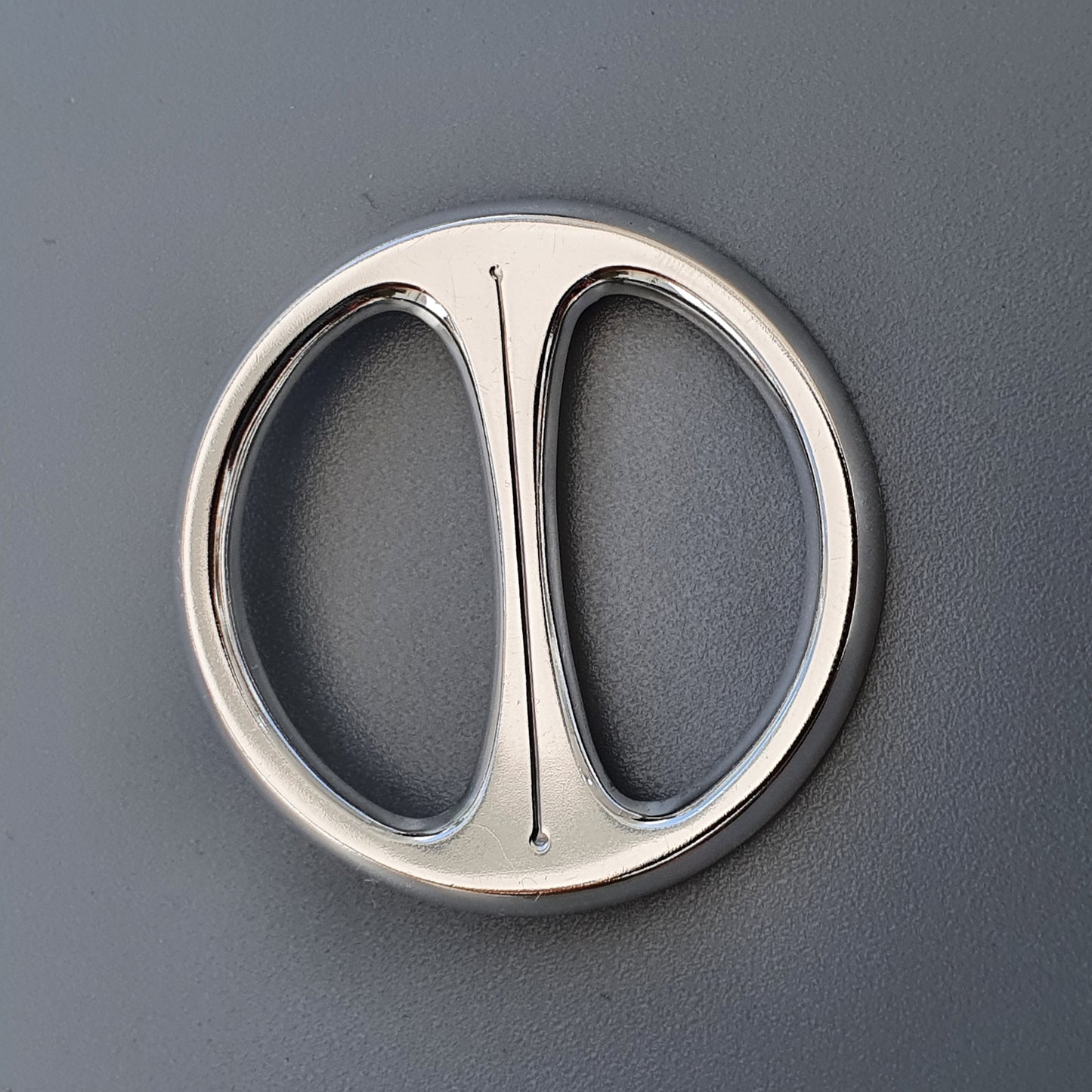 Circular metal belt buckle with a central divider creating two semicircular openings.