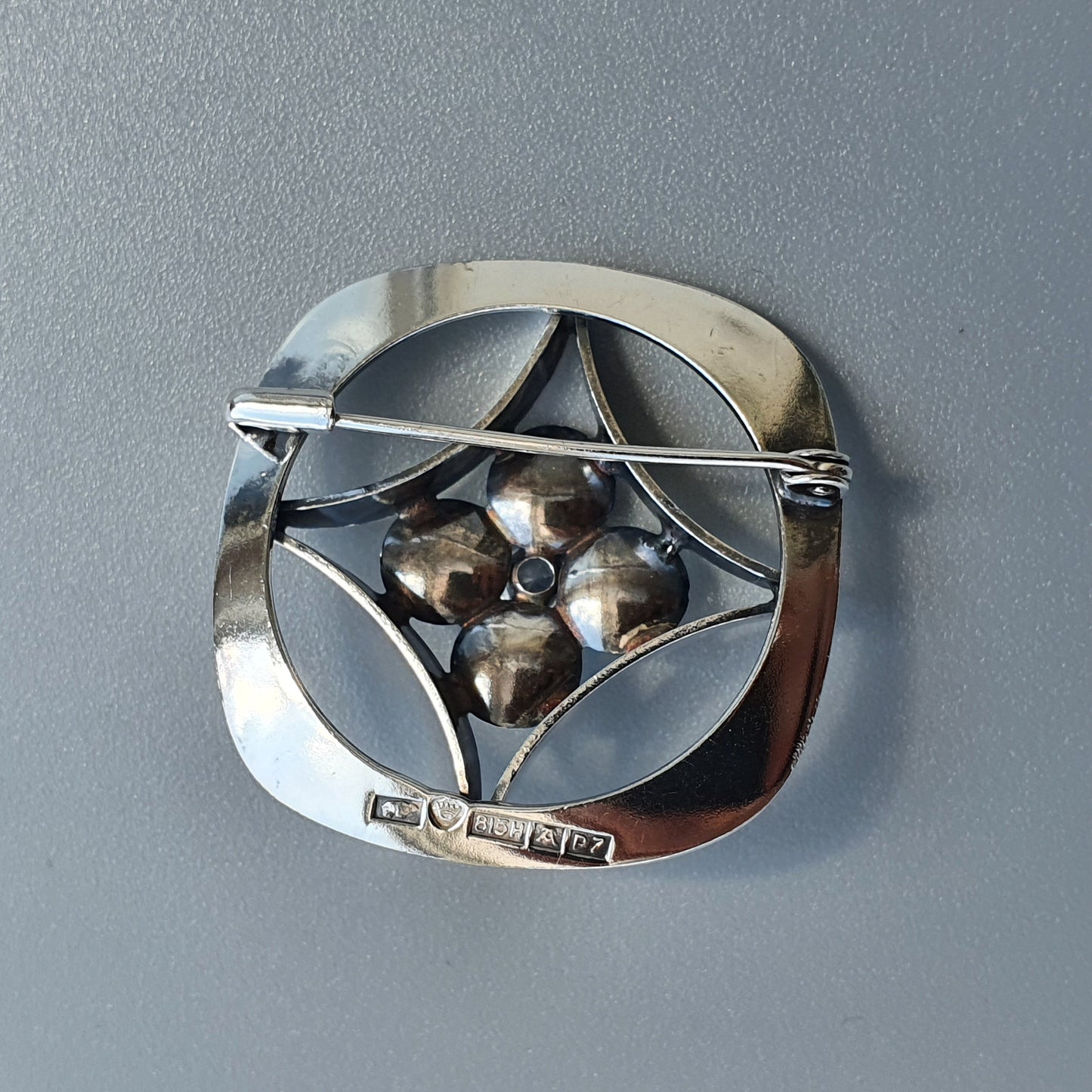 Silver brooch with a geometric design featuring four spherical elements at its center.