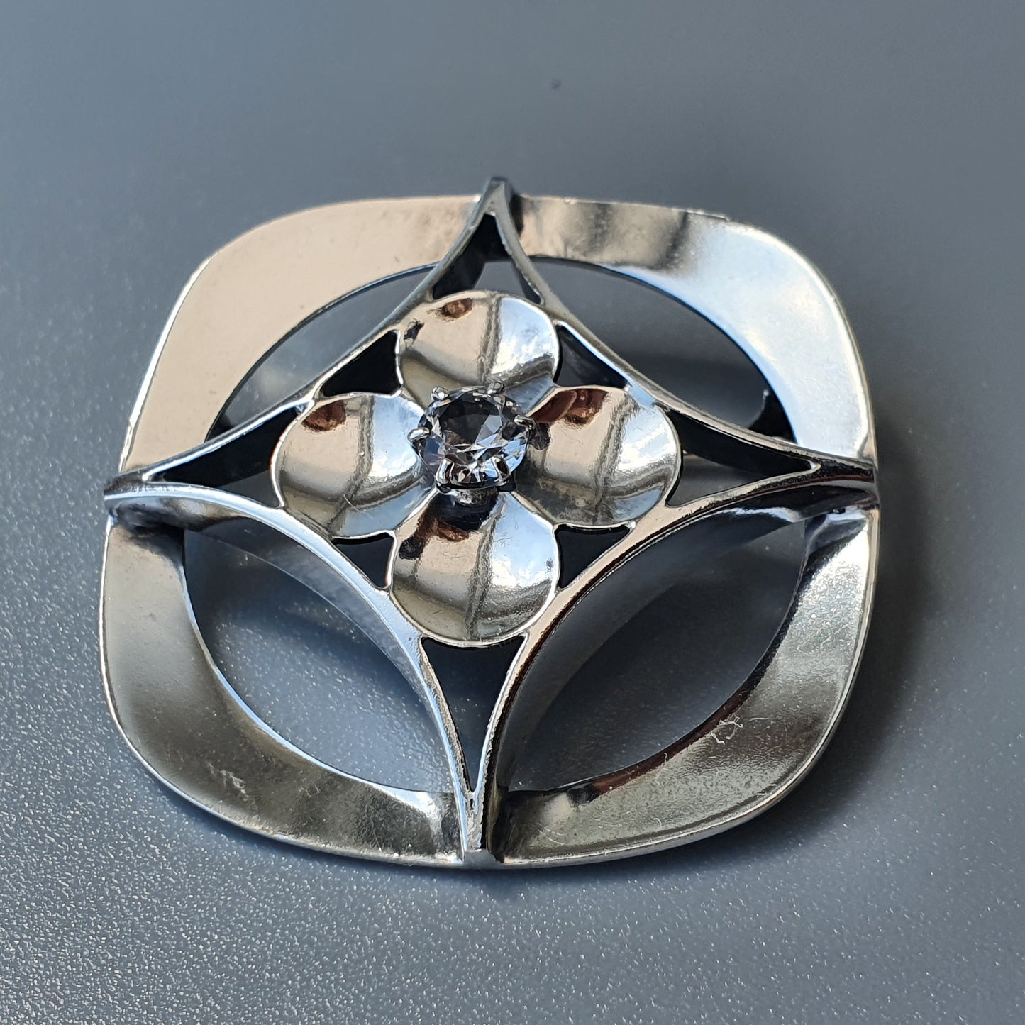 Decorative silver brooch with a floral design featuring petals and a central gem.