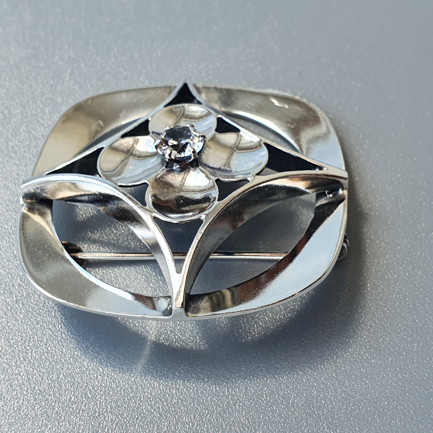 Silver brooch or pendant with a geometric floral design and a central gemstone.