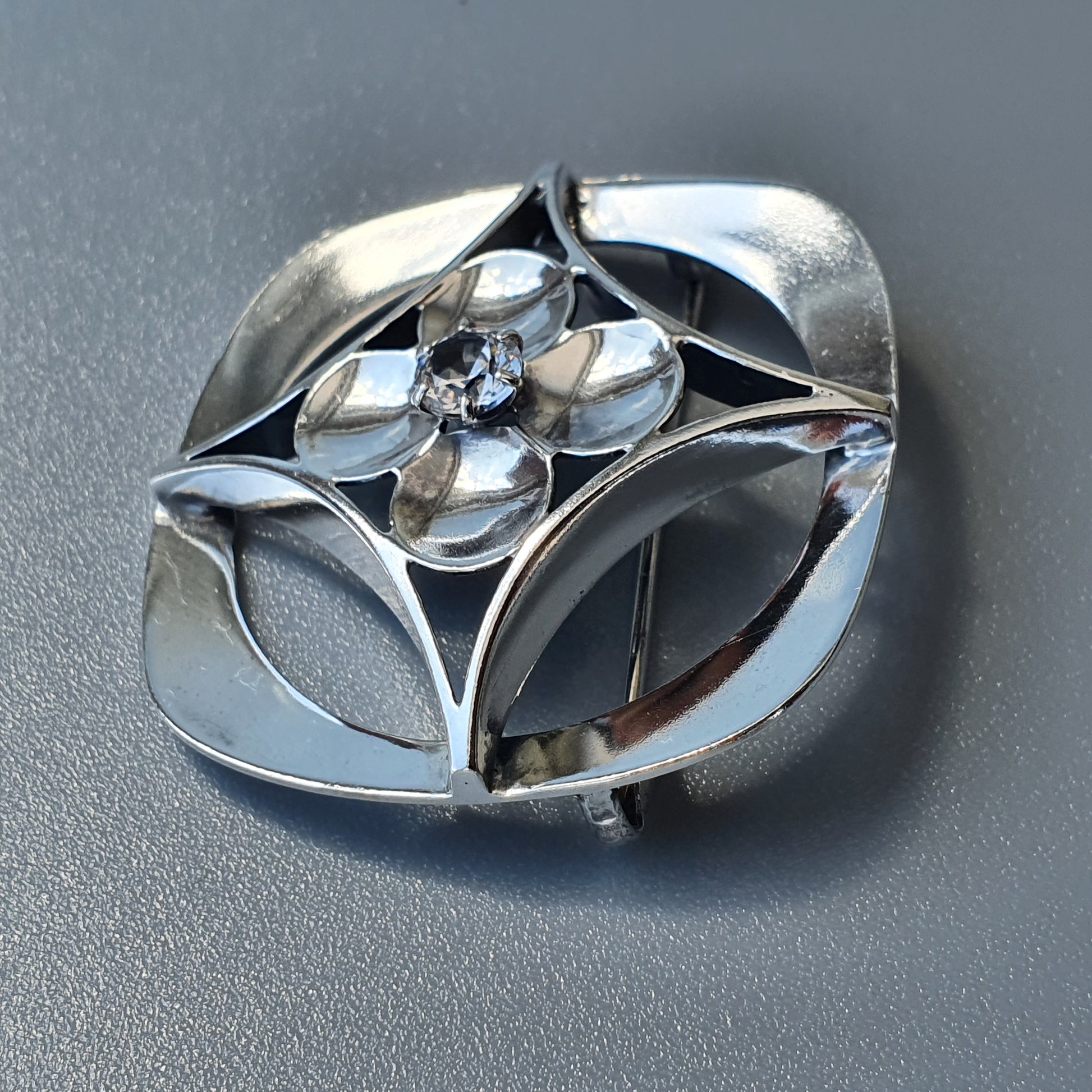 Silver brooch or pendant with an abstract floral or geometric design featuring curved shapes and a central crystal or gemstone.