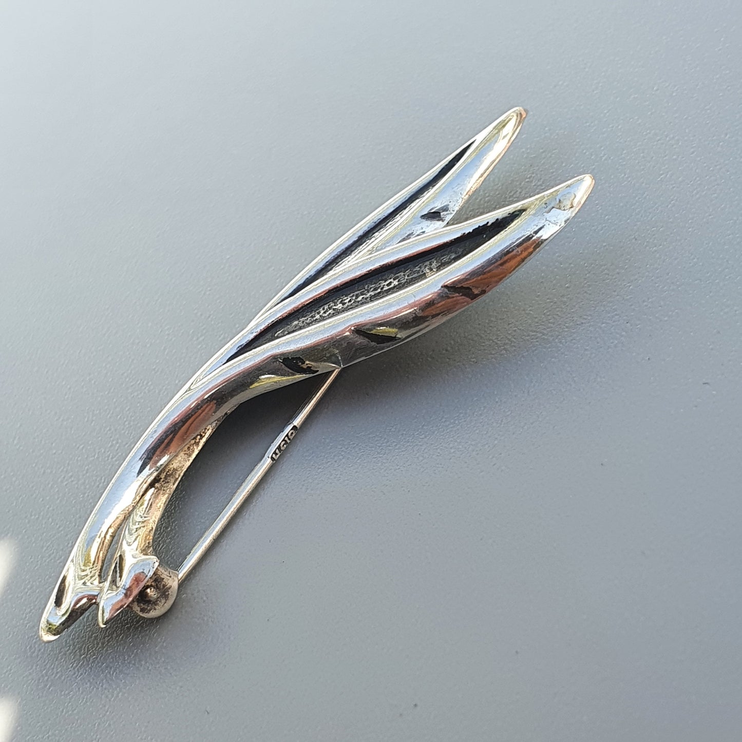 Sleek, elongated chrome hood ornament with a stylized wing or fin design.