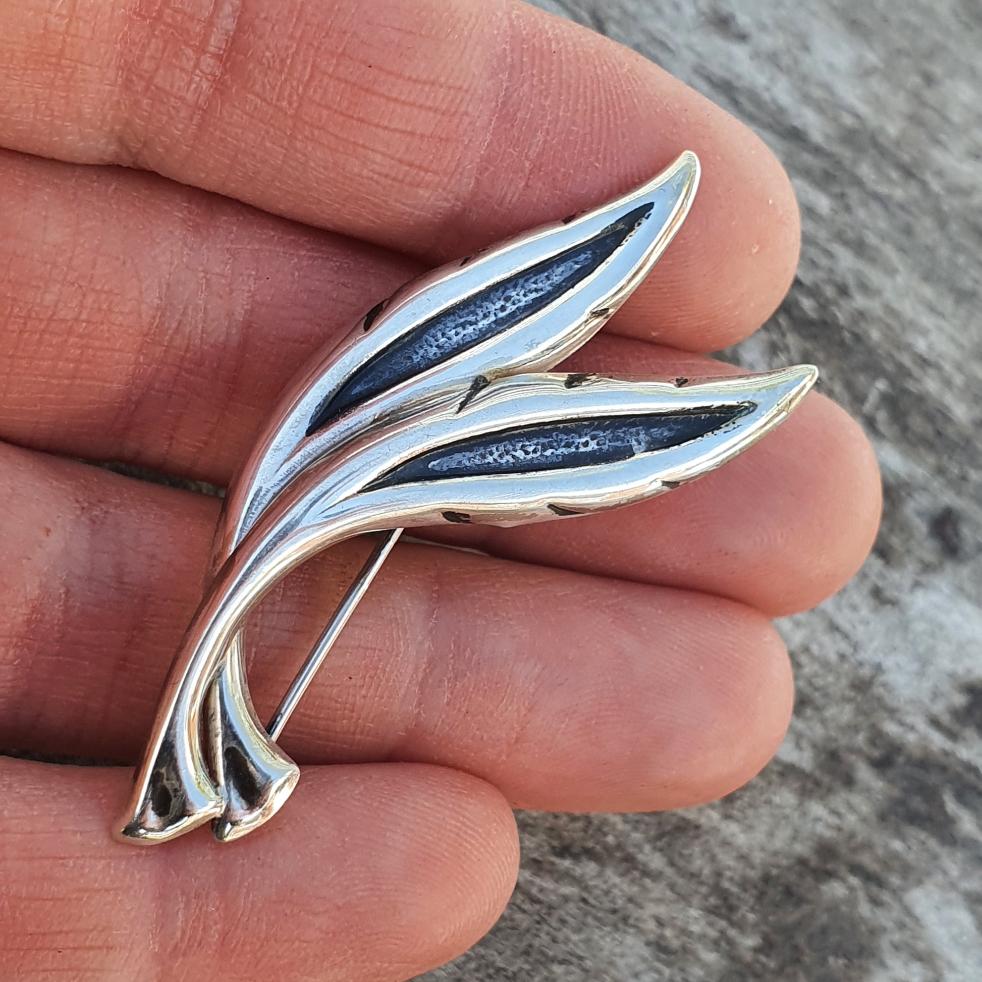 Silver brooch or pin shaped like a stylized leaf or feather with dark blue enamel inlays.