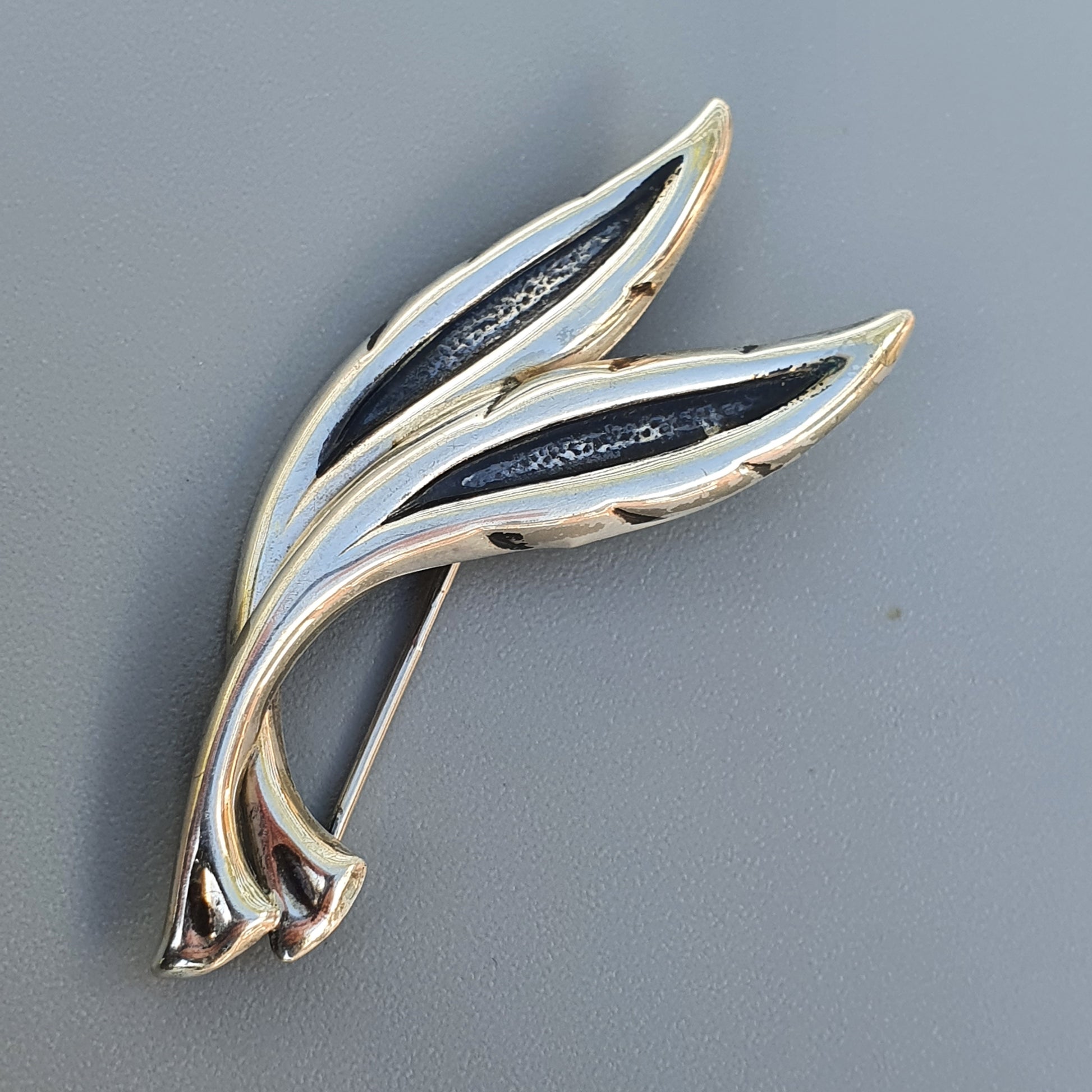 Stylized leaf-shaped brooch or pin with gold-toned edges and dark inlaid sections.