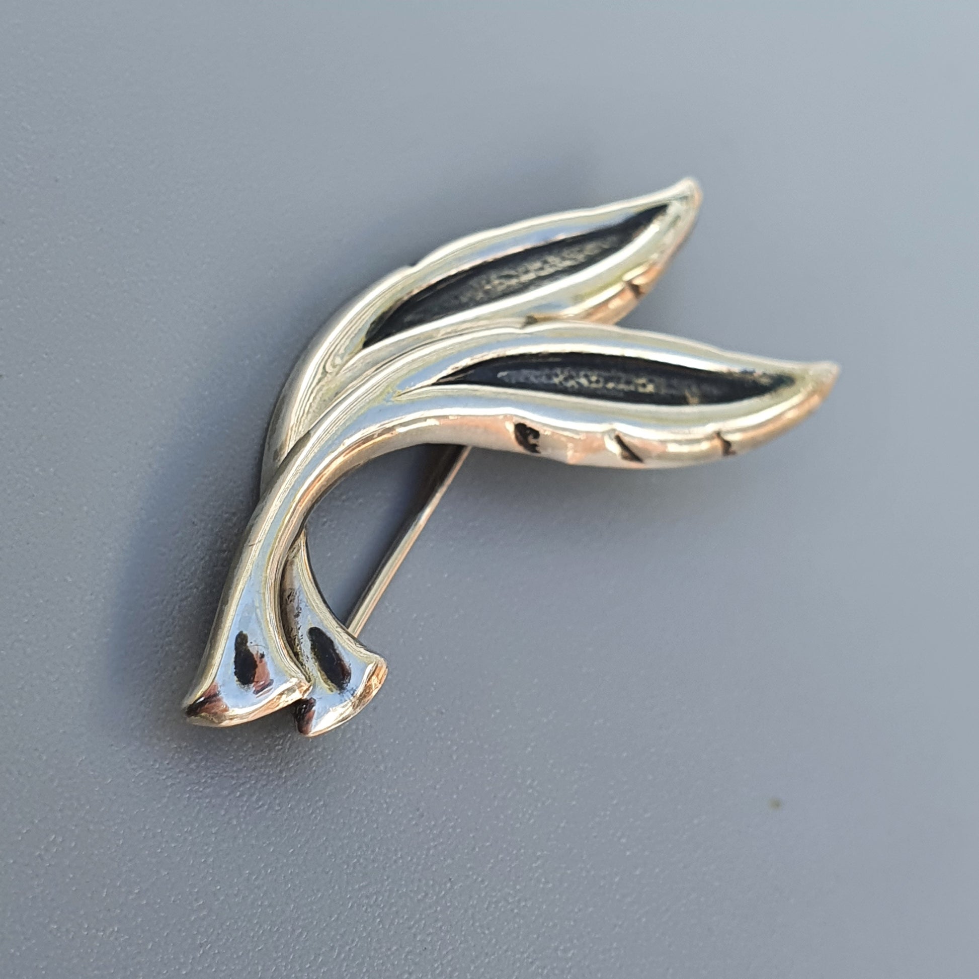 Stylized silver brooch or pin shaped like an abstract dolphin or fish.