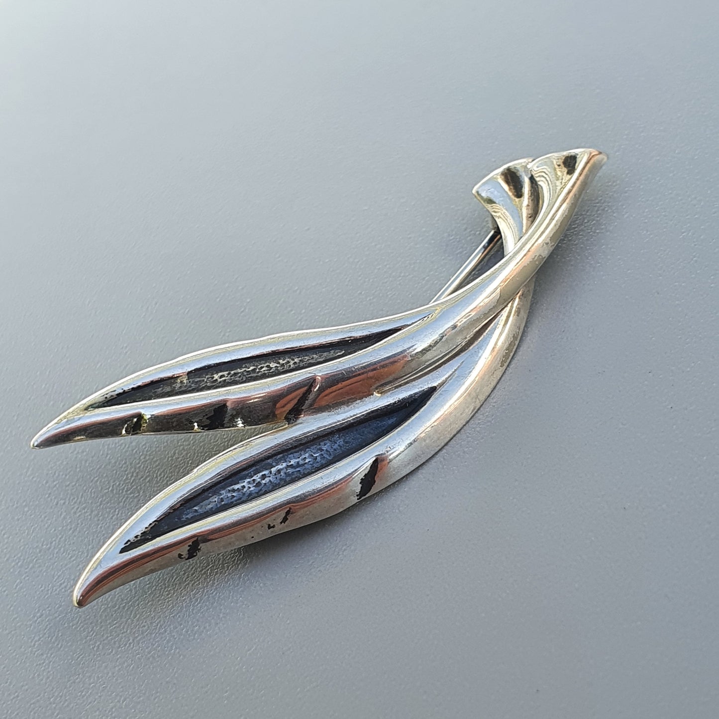 Sleek silver brooch or pin shaped like stylized leaves or feathers.