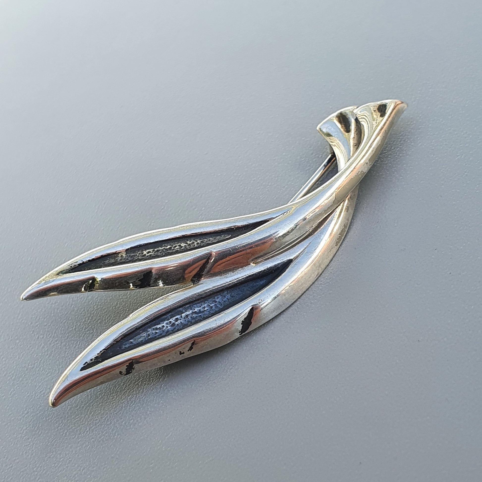 Sleek silver brooch or pin shaped like stylized leaves or feathers.