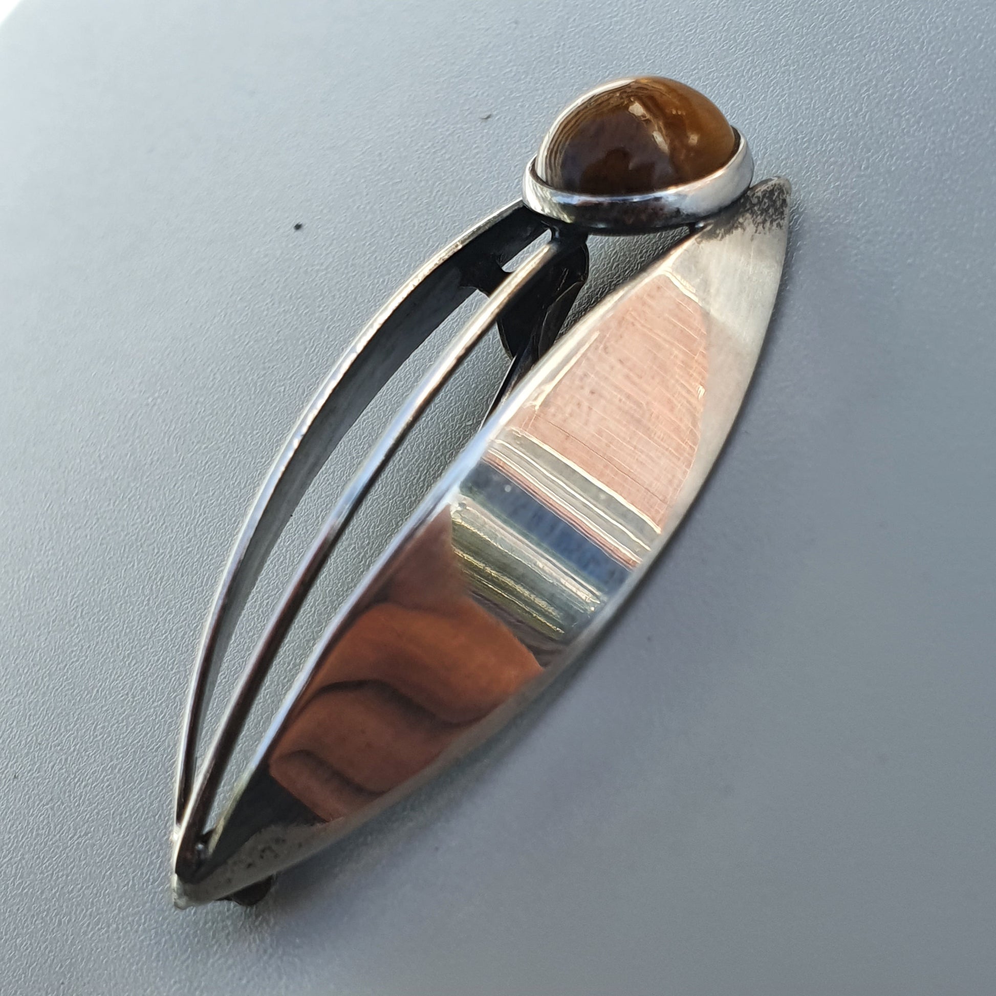 Sleek silver pendant with a brown gemstone set in an oval design.