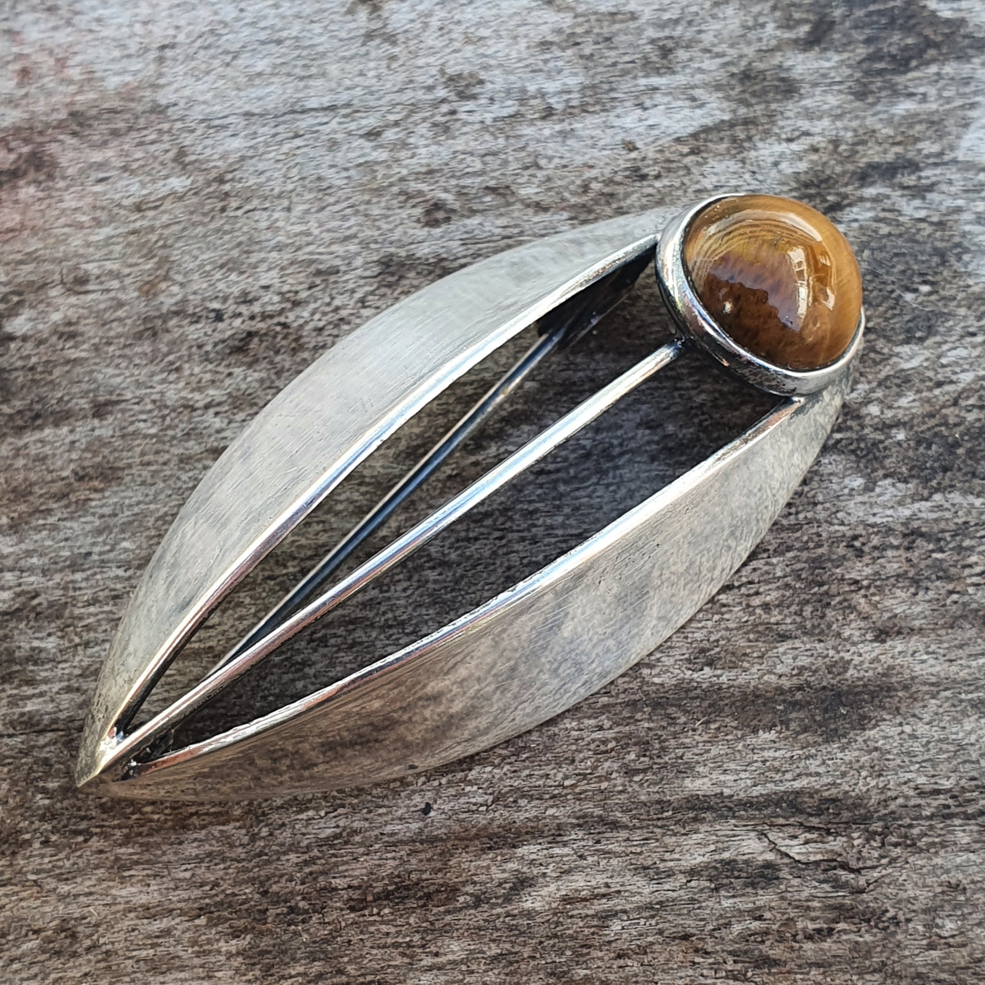 Silver leaf-shaped brooch or pendant with a round amber-colored stone set at one end.