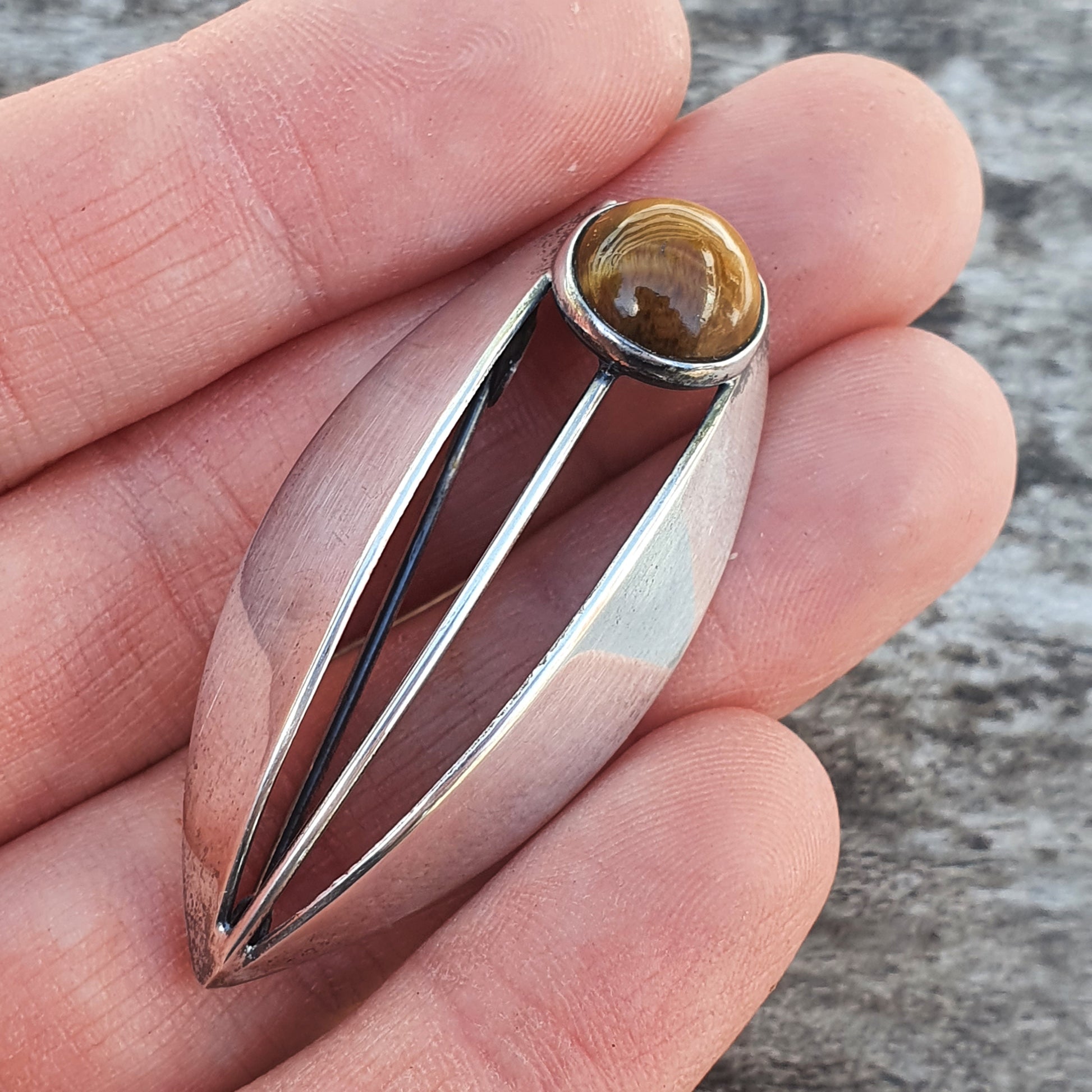 Sleek silver pendant with an elongated teardrop shape and a round amber-colored stone at the top.