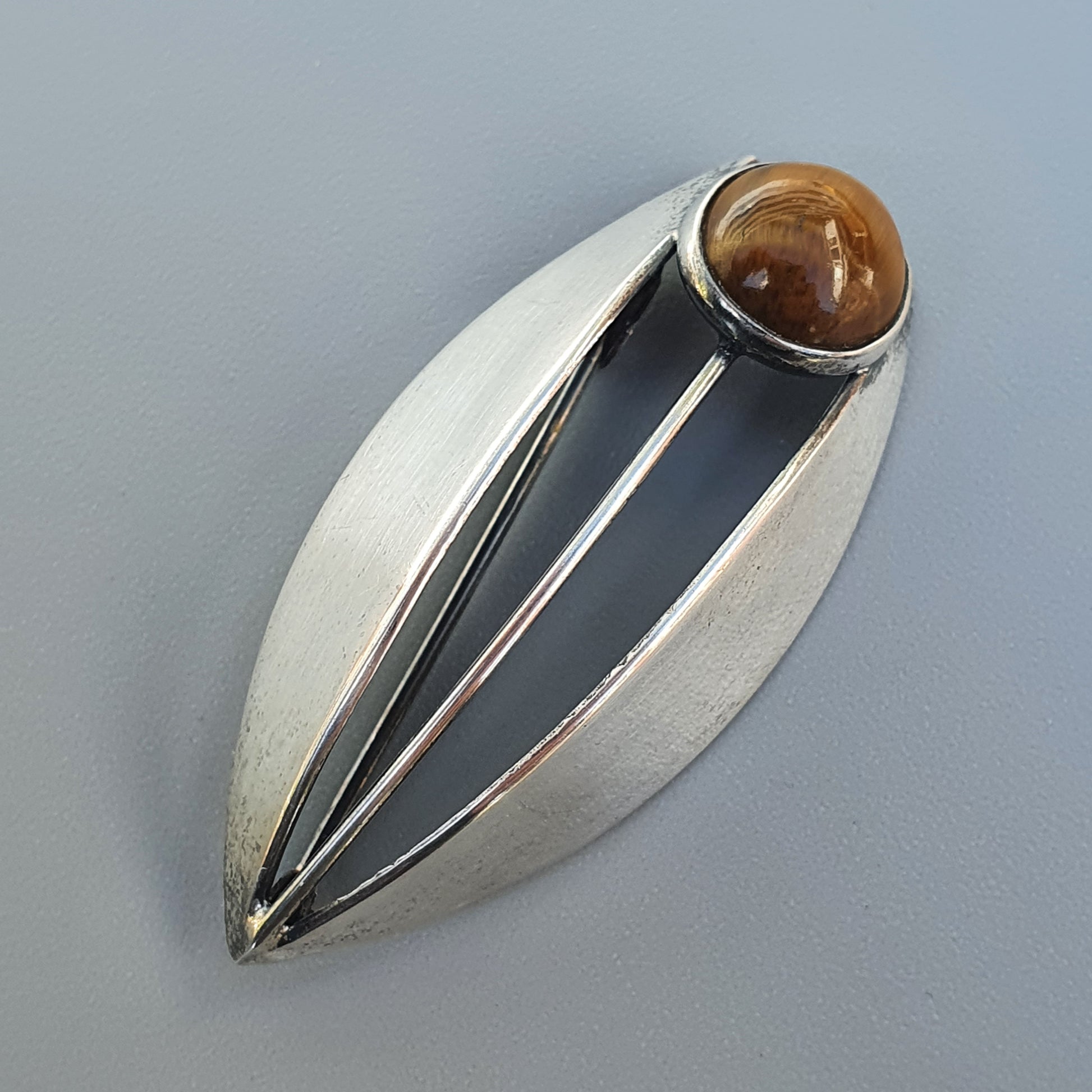 Leaf-shaped silver brooch with a brown gemstone at one end.