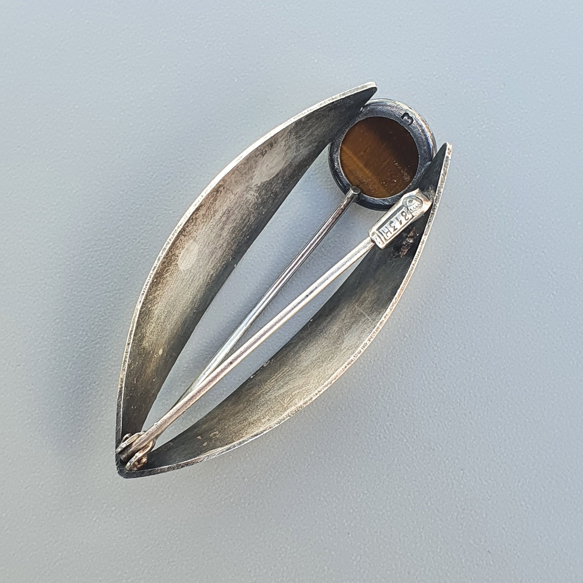 Modernist silver brooch with an oval shape and amber-colored stone accent.