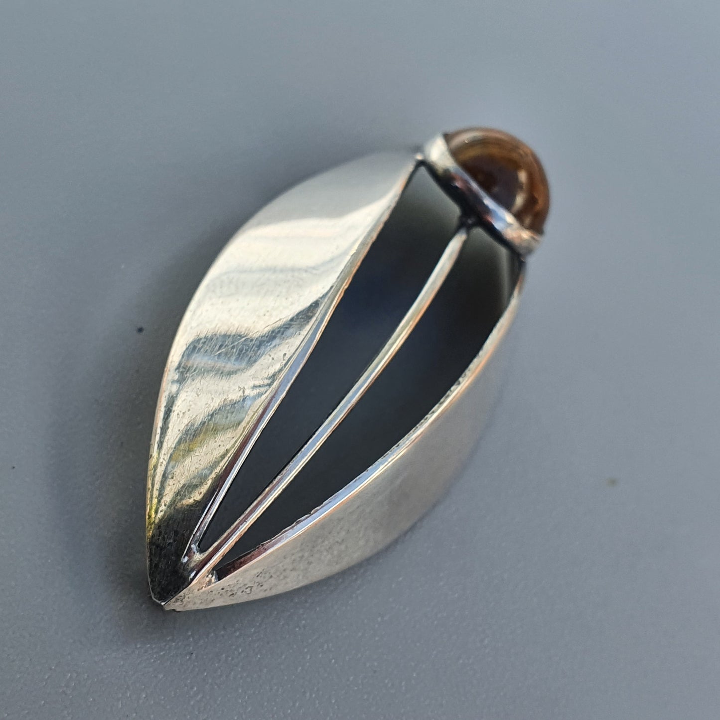 Leaf-shaped silver pendant with a dark inlay and central wire detail.