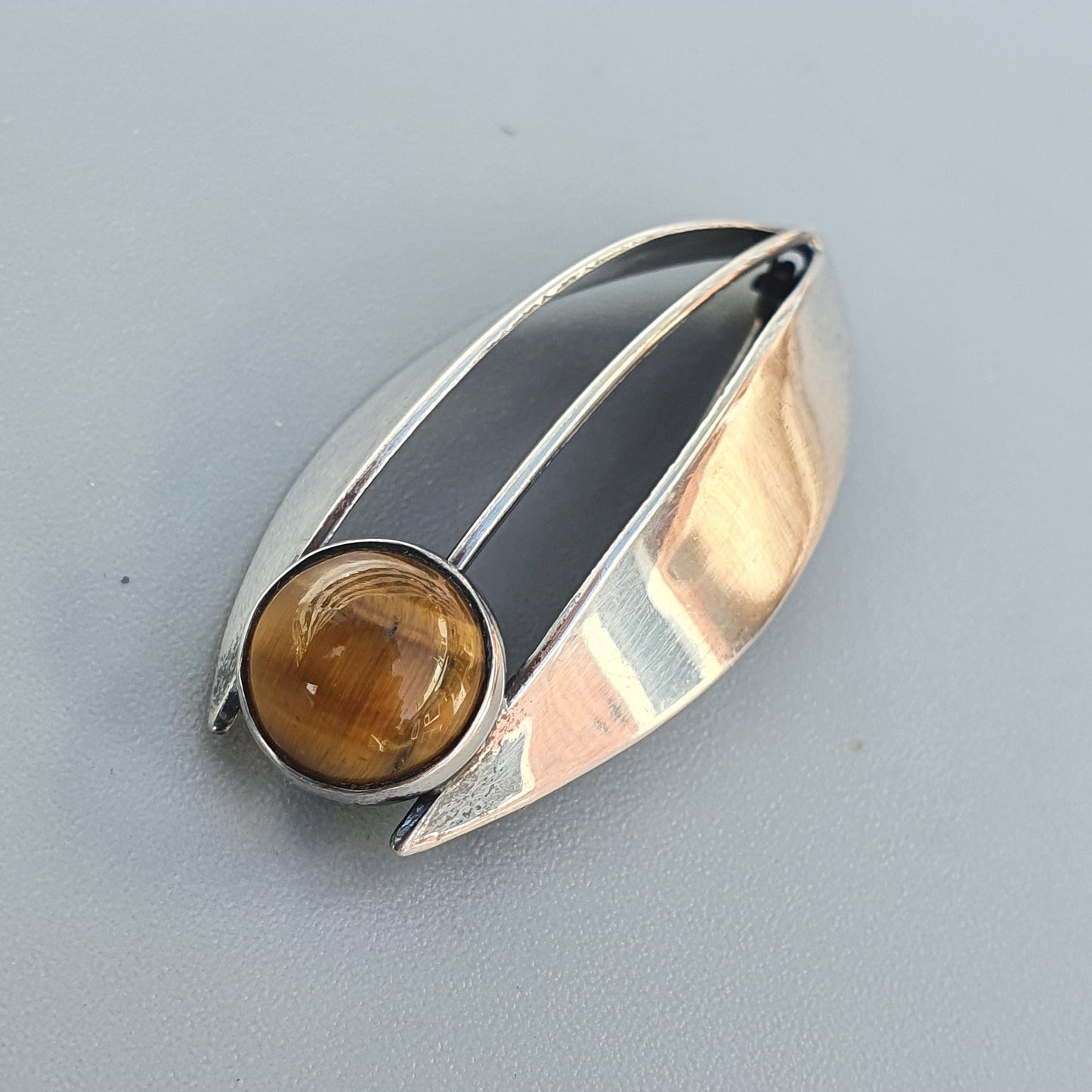 Modernist silver brooch with a leaf-like shape featuring black enamel and an amber-colored gemstone.