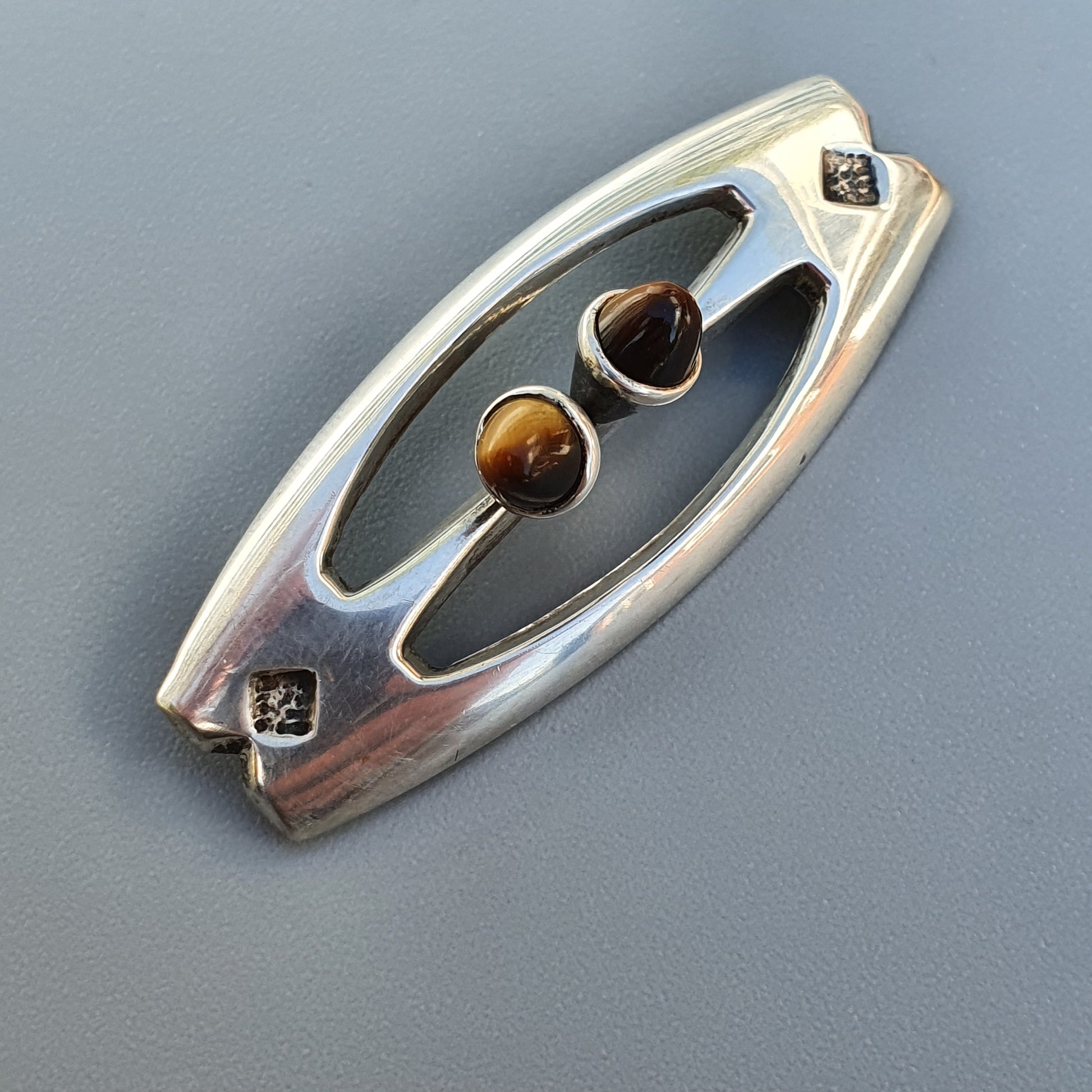 Oval-shaped silver brooch or pendant with two tiger’s eye gemstones set in an open design.