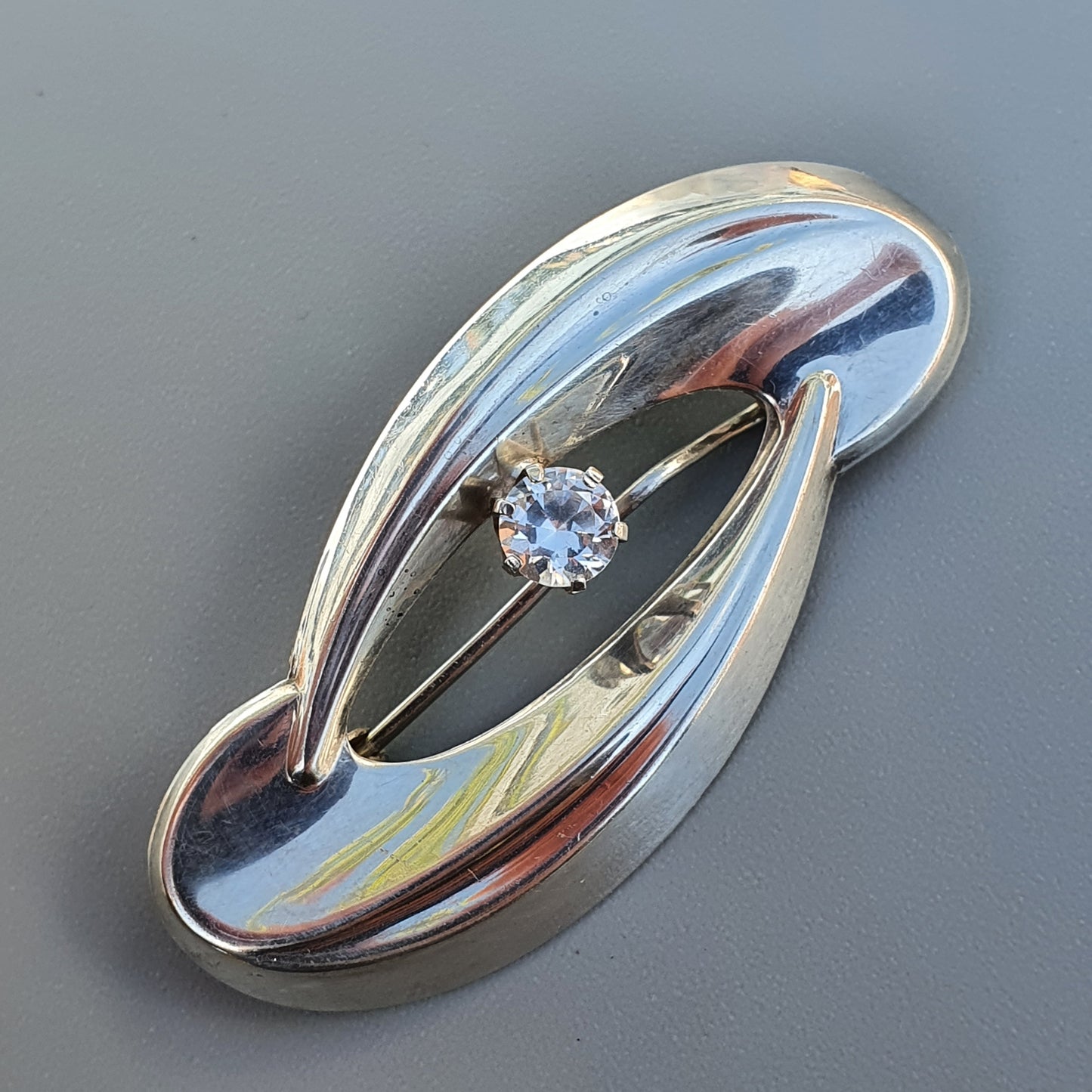 Elegant silver brooch with a curved design and central gemstone.