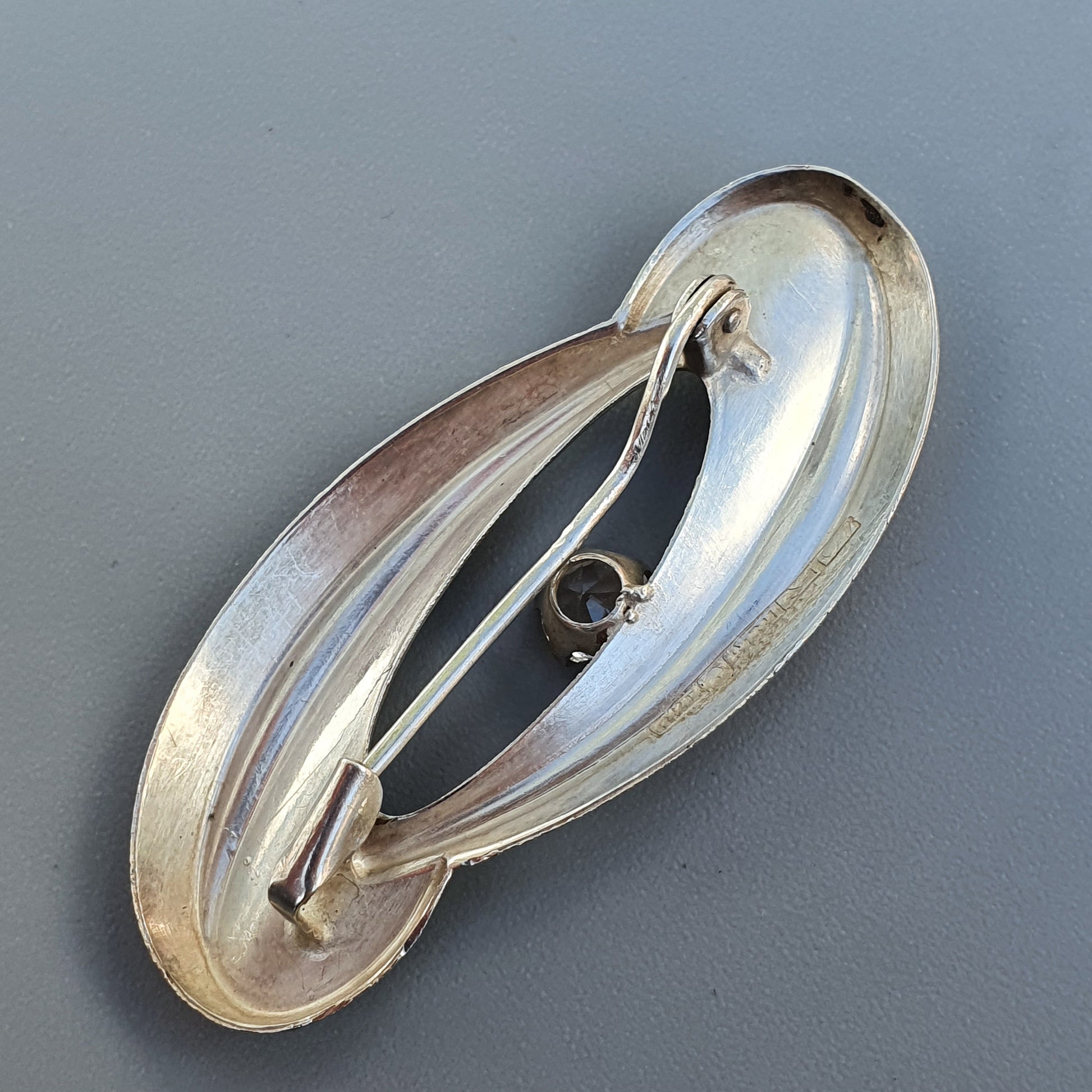 Oval-shaped silver brooch or pin with an abstract, curved design.