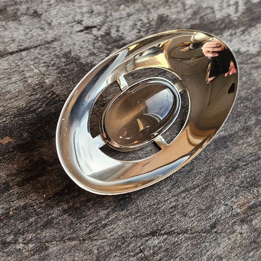 Shiny metallic oval-shaped object with a circular indentation in the center.