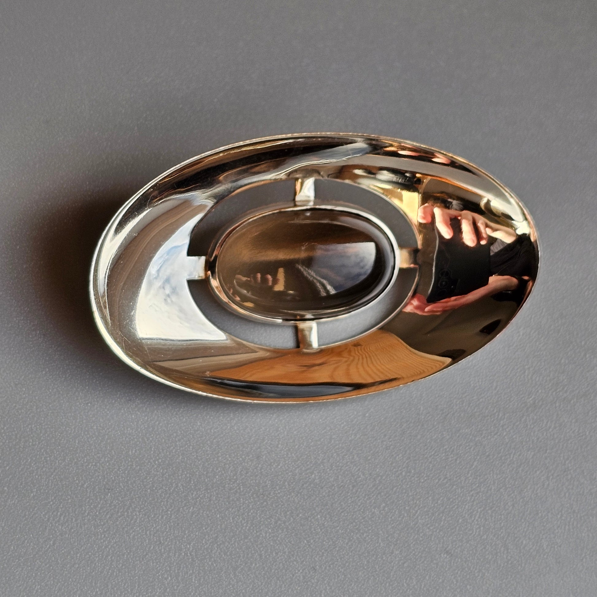 Shiny metallic ashtray with a circular indentation and curved edges.