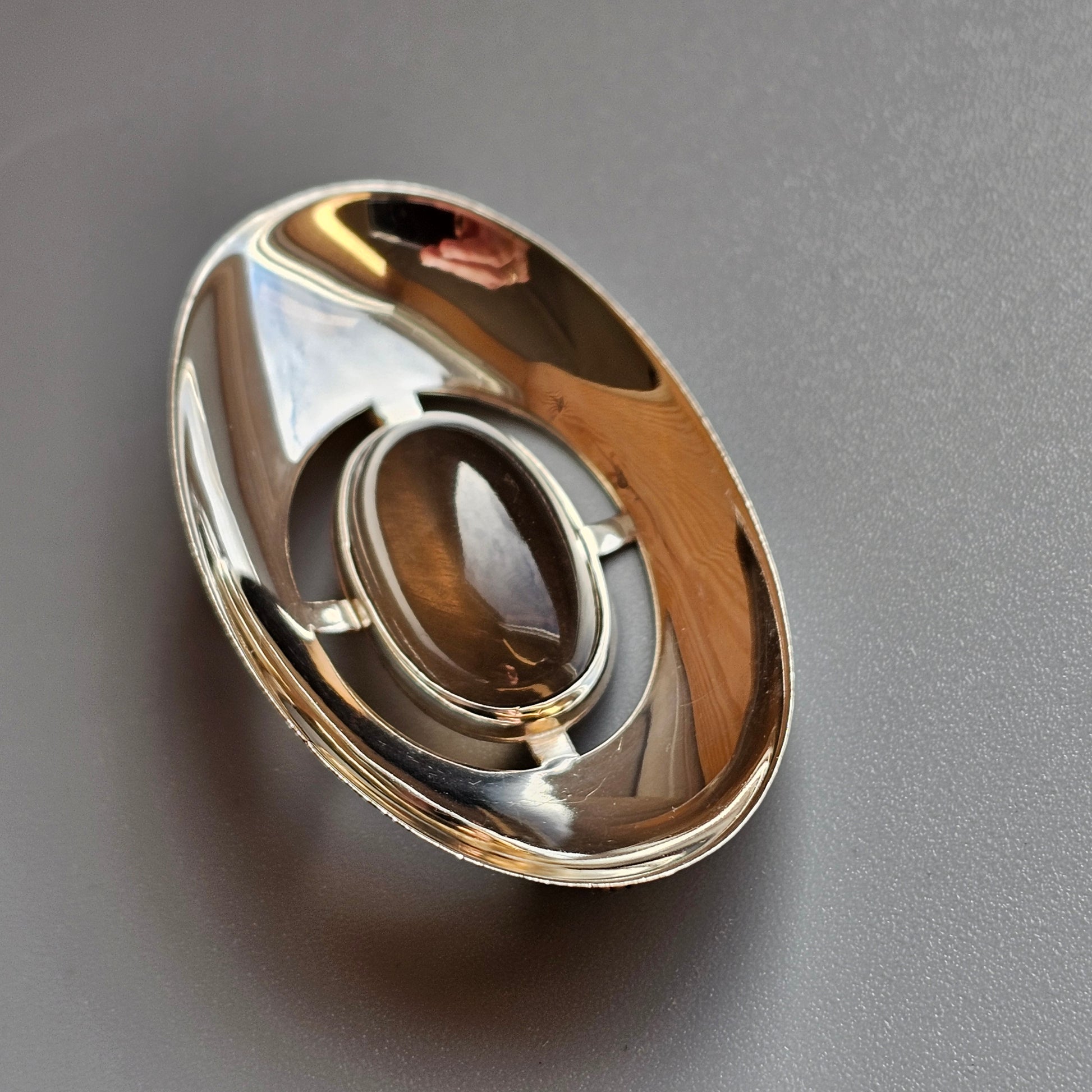 Oval-shaped metallic object with a central opening and reflective surfaces.