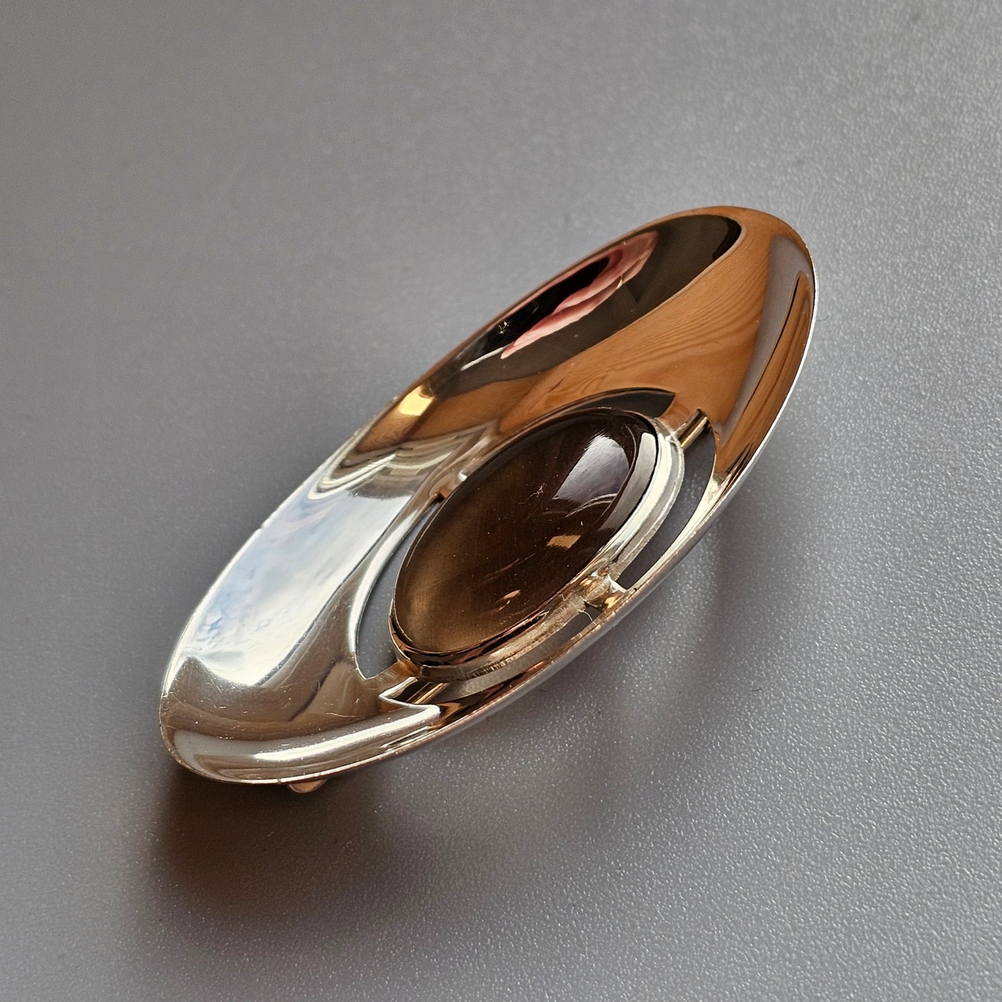 Oval-shaped metallic object with smooth, reflective surfaces and curved contours.